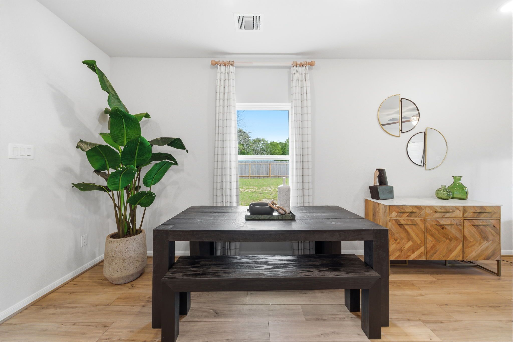 Spacious dining room with rustic wooden table, benches, large potted plant, gold mirrors, and yard view window at Caney Creek Place in Conroe Texas