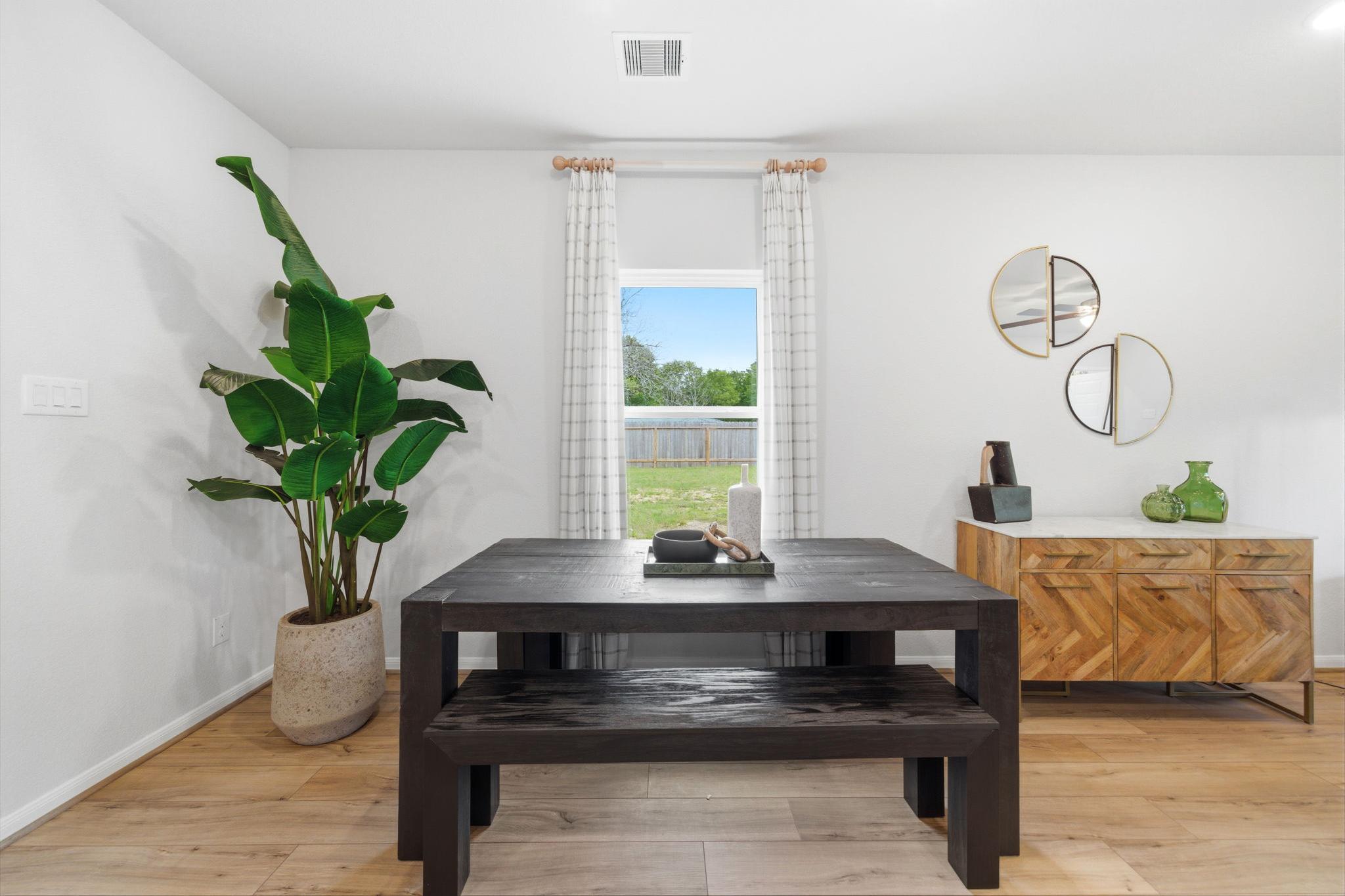 Spacious dining room with rustic wooden table, benches, large potted plant, gold mirrors, and yard view window at Caney Creek Place in Conroe Texas