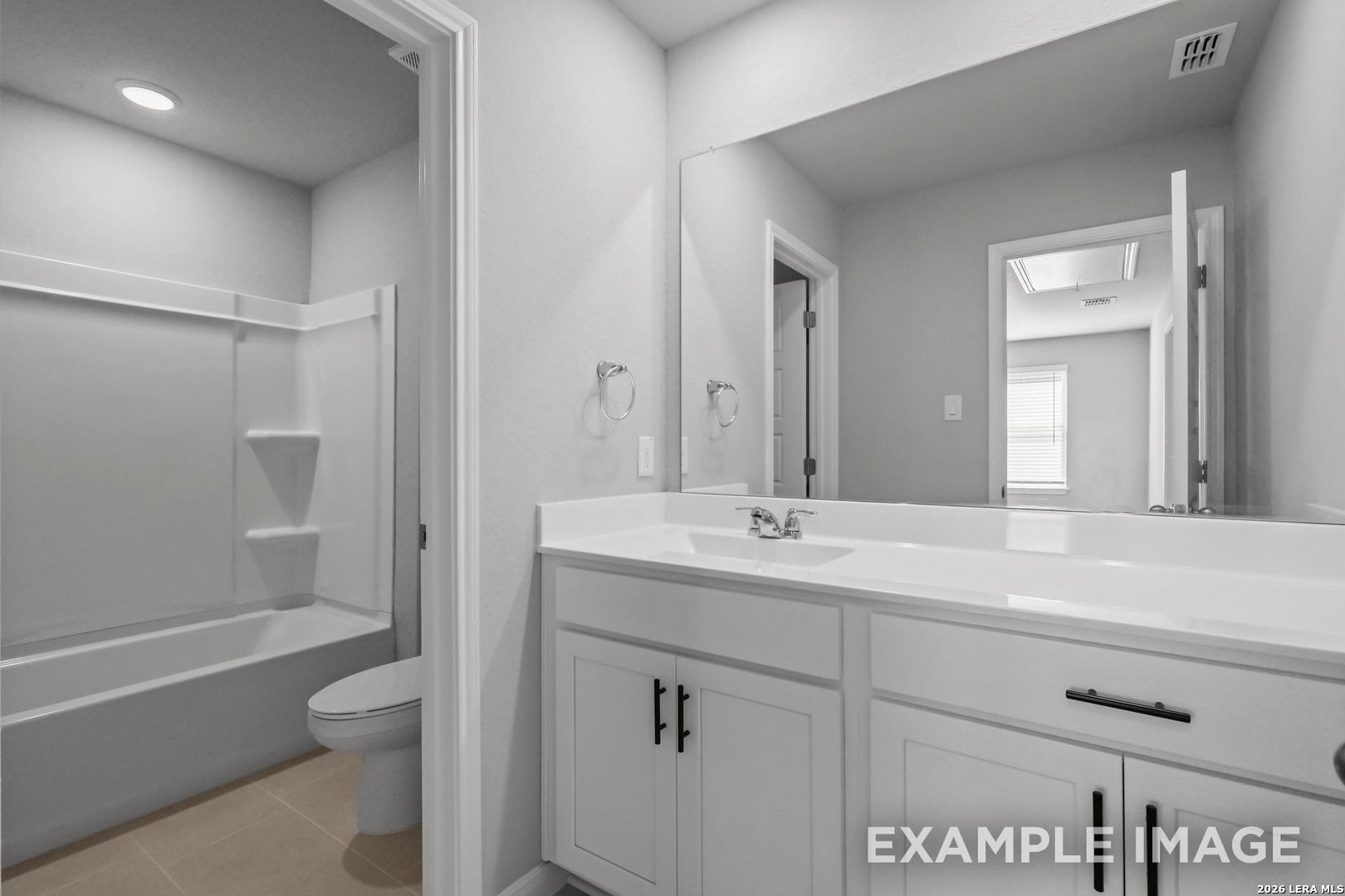 Modern bathroom with white vanity, large mirror, and tub-shower combo in The Gillian A home, Cedar Heights, San Antonio.