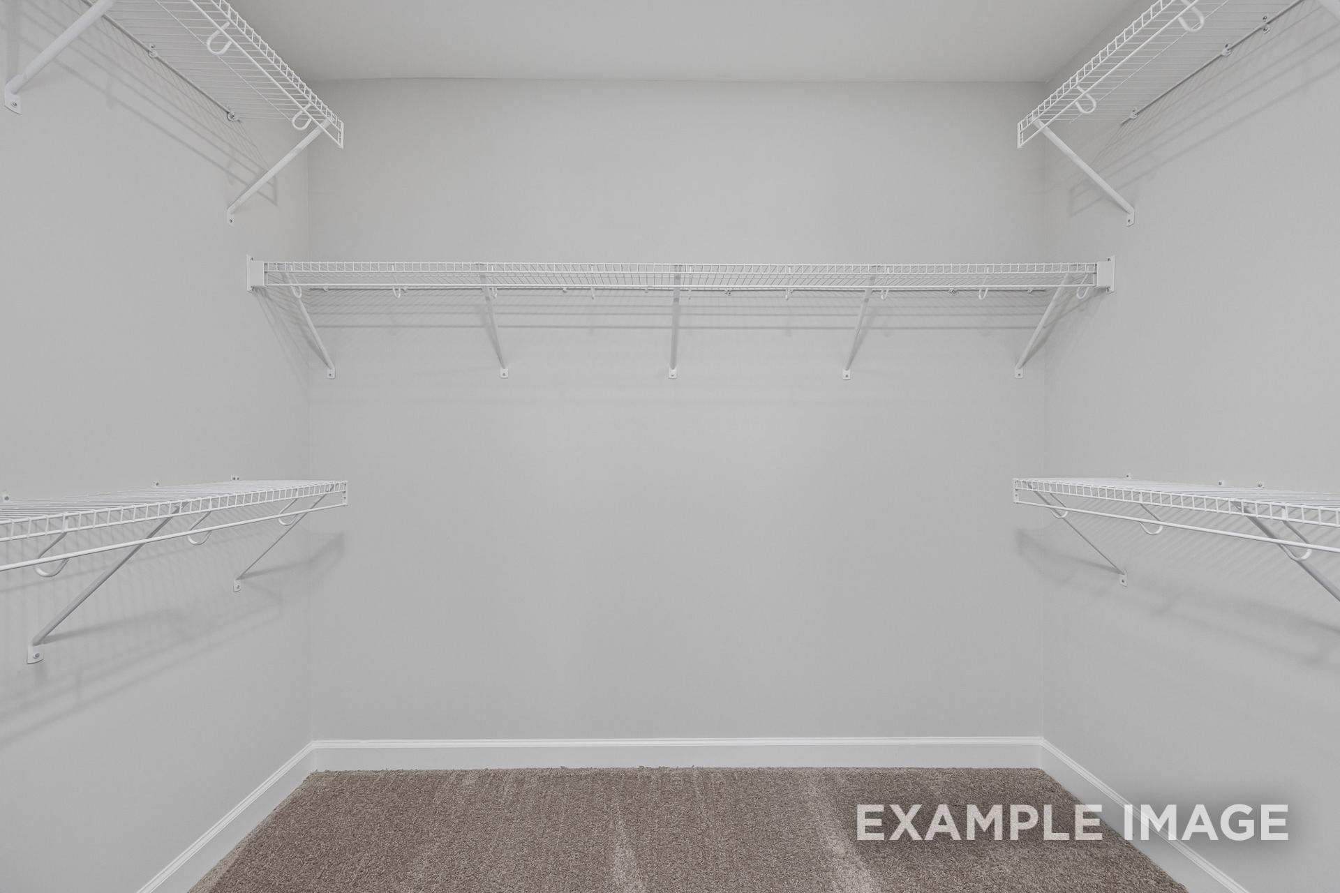 Spacious walk-in closet in The Adalynn C master suite featuring white wire shelving, hanging rods, light gray walls, brown carpet