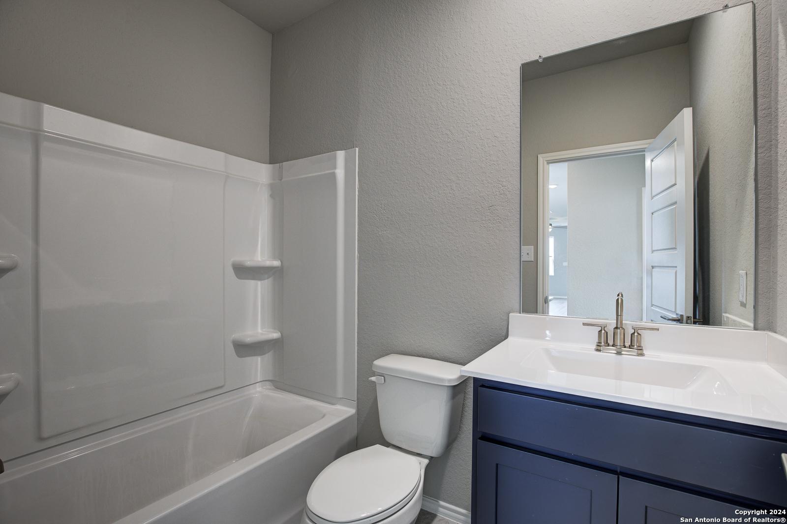 Modern bathroom with white tub-shower combo, navy vanity, and toilet in Davidson Homes The Frio B, San Antonio, Texas