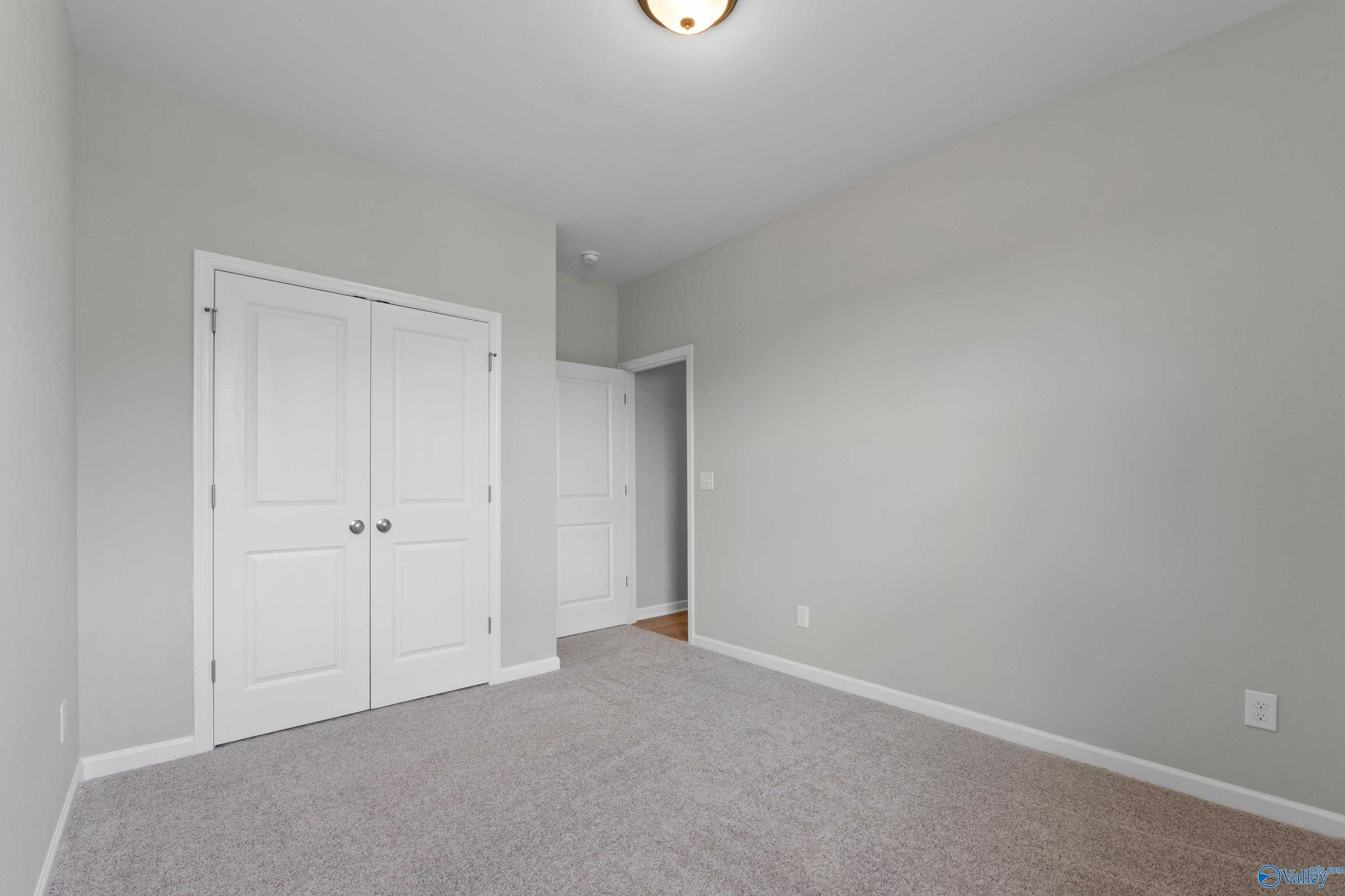 Spacious secondary bedroom featuring gray walls, white double closet doors, and plush carpet in Evermore Homes The Aurora, Harvest AL