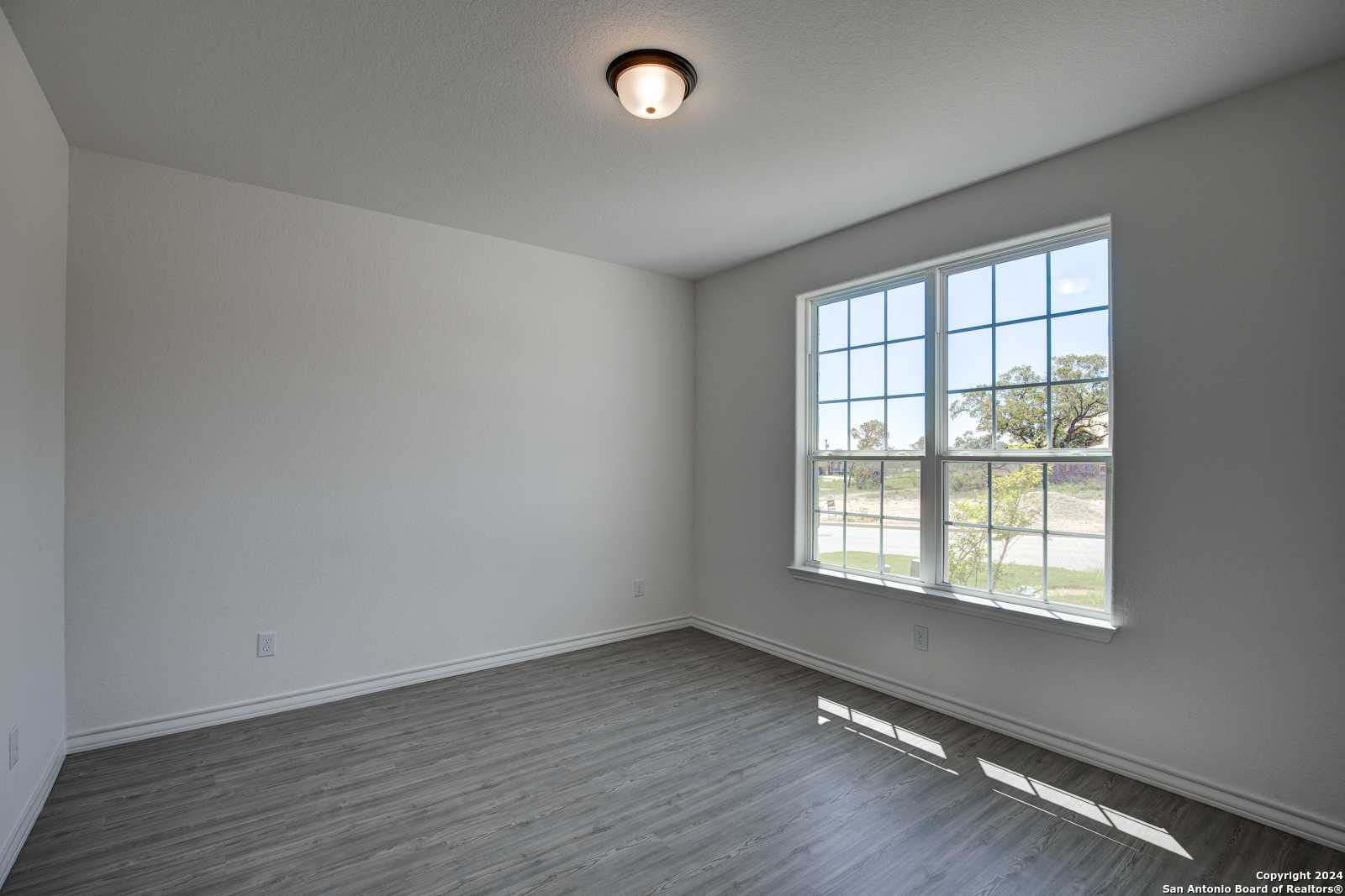 Bright secondary bedroom with large window, gray walls, and hardwood floors in The Garner B, Davidson Homes, Castroville, Texas
