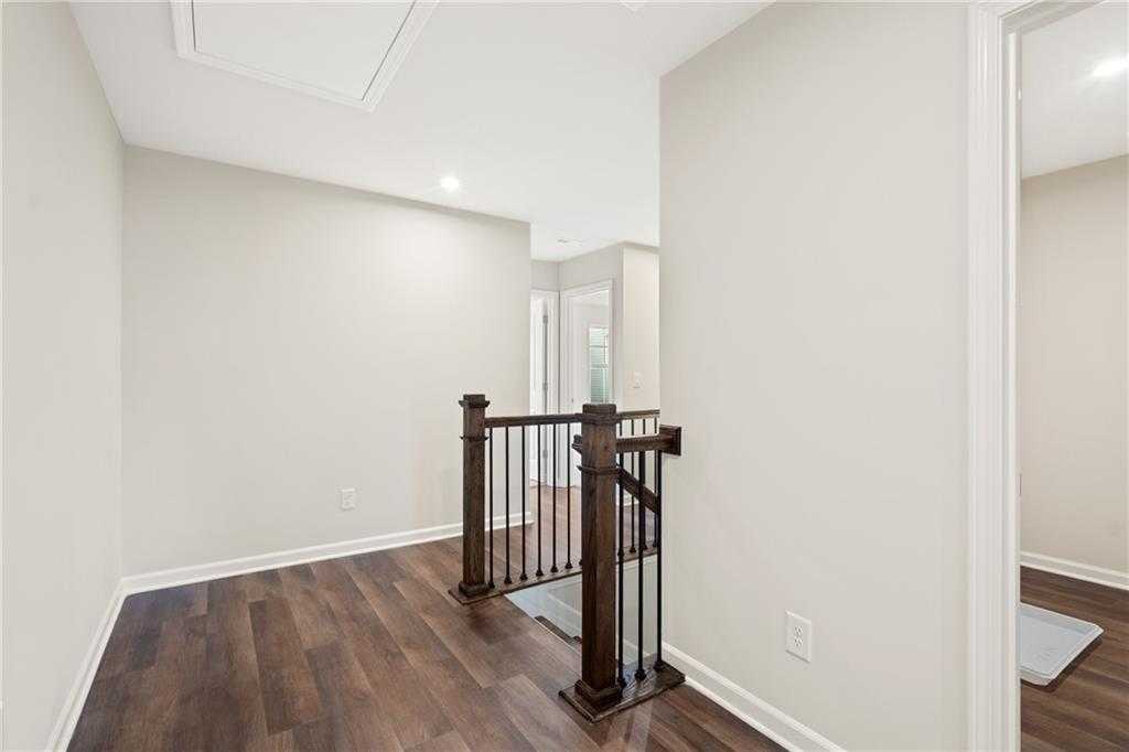 Upper-level hallway with wooden staircase railing, metal balusters, light gray walls, and hardwood floors in Davidson Homes The Cary B, Kennesaw, GA