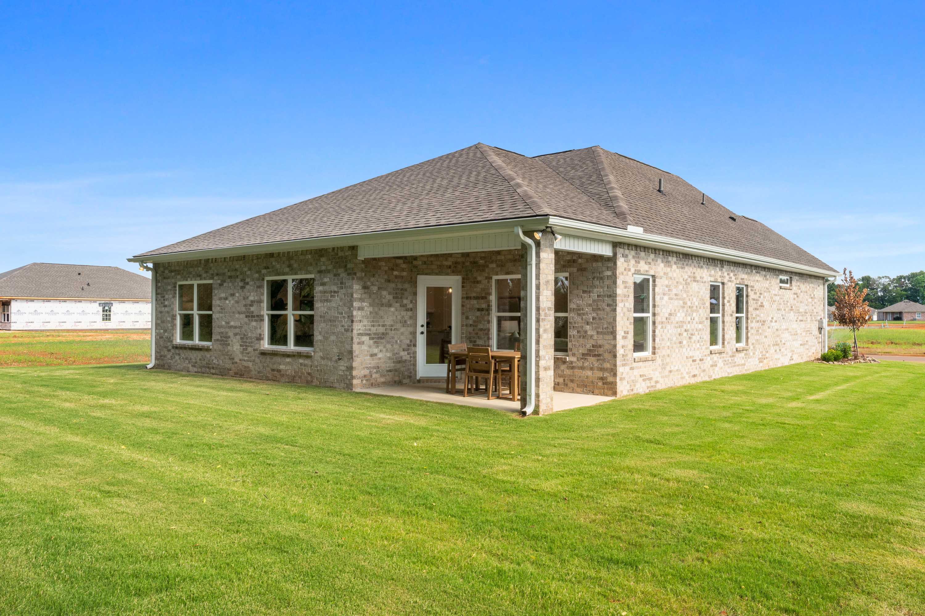 Brick home side exterior with covered patio, French doors, bistro seating and lush green lawn at Lynn Meadows in Meridianville, Alabama
