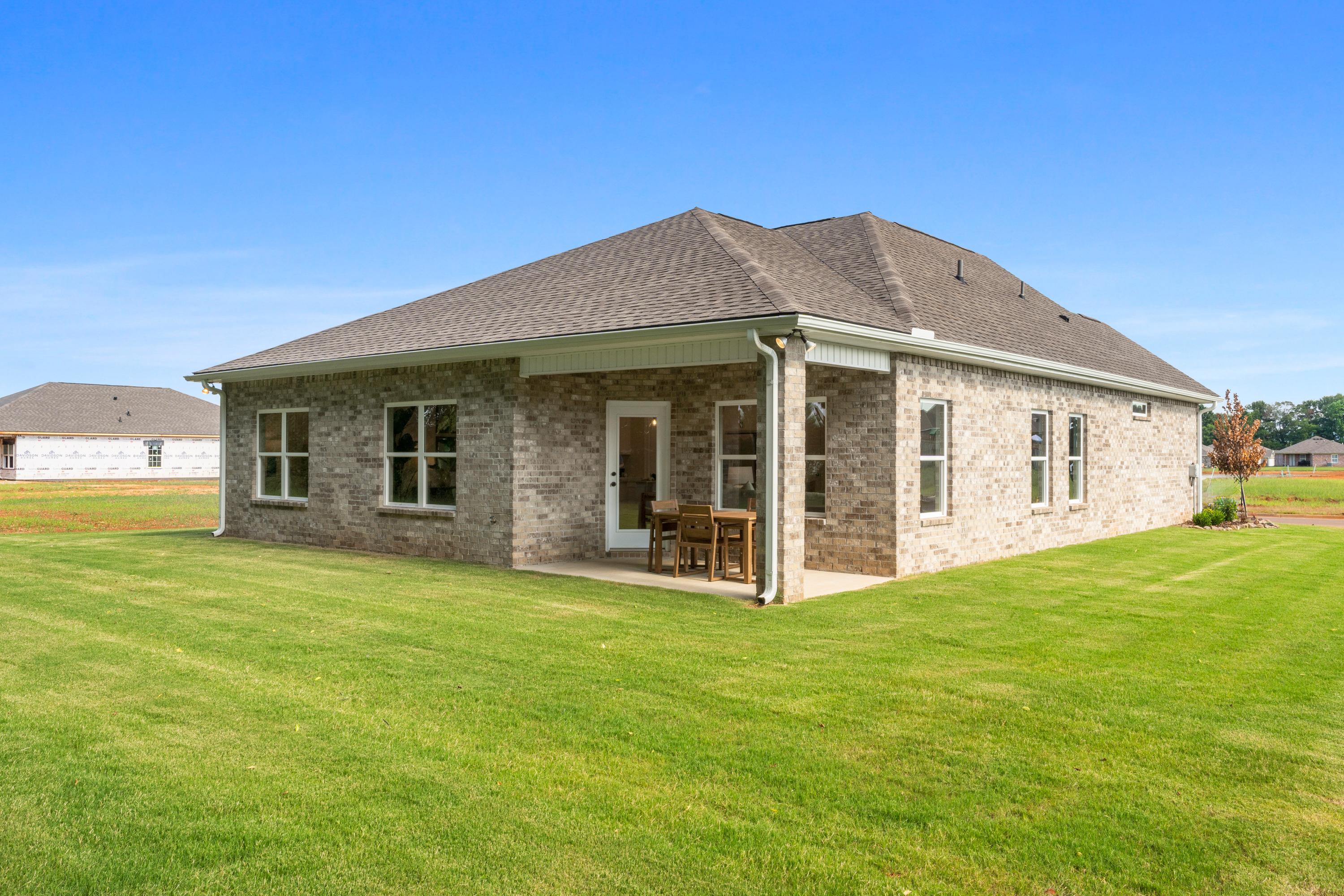 Brick home side exterior with covered patio, French doors, bistro seating and lush green lawn at Lynn Meadows in Meridianville, Alabama