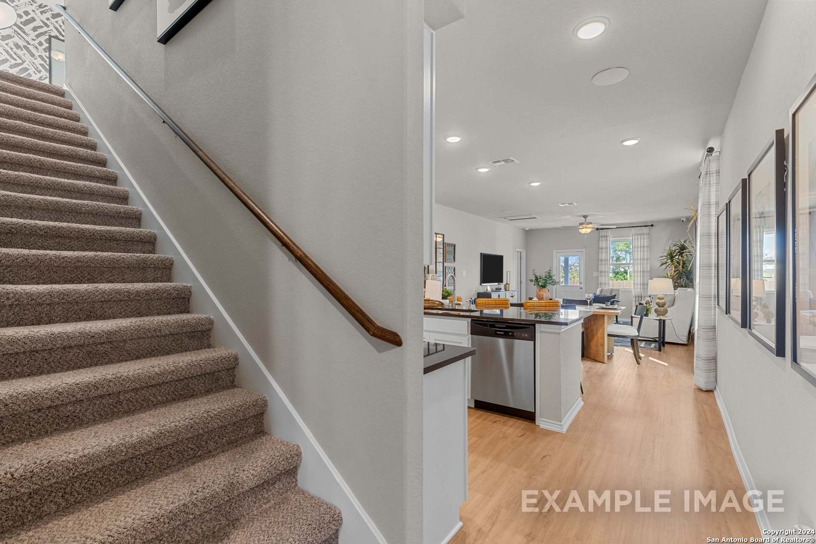 Open kitchen with white cabinets and island adjacent to carpeted staircase in The Sabine B 4-bedroom home, San Antonio, Texas