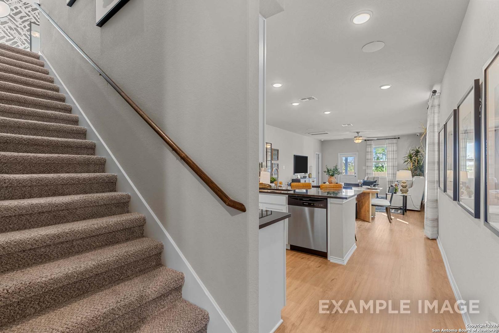 Open kitchen with white cabinets and island adjacent to carpeted staircase in The Sabine B 4-bedroom home, San Antonio, Texas