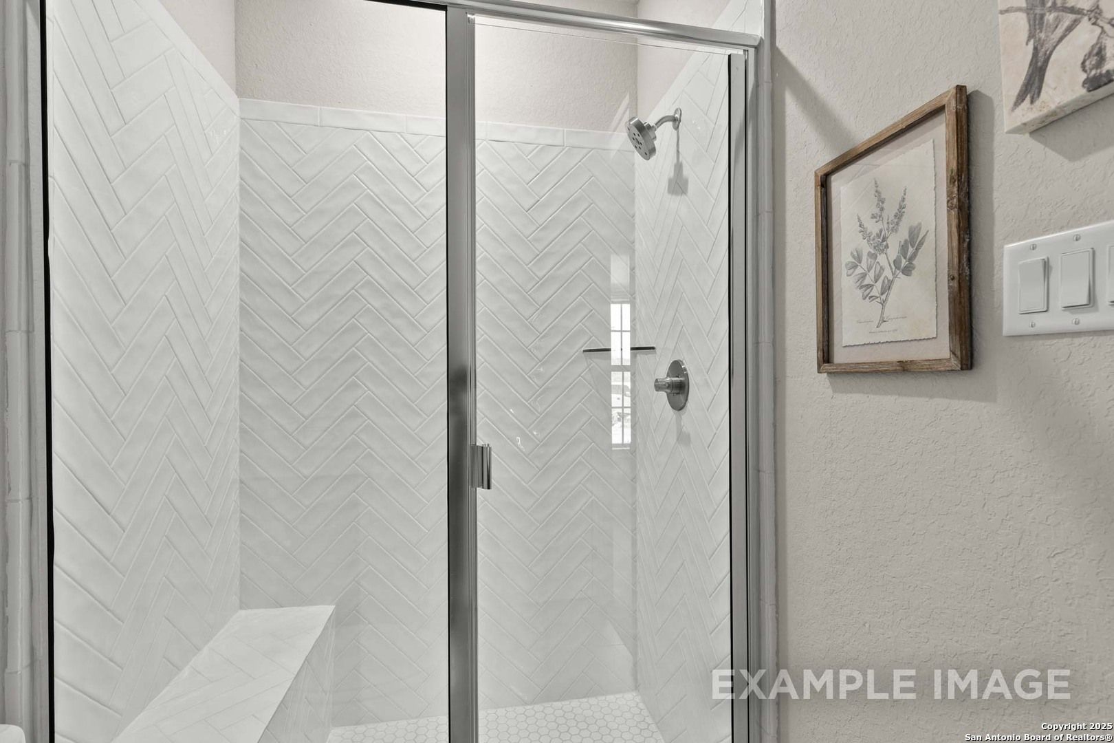 Elegant frameless glass shower with white herringbone tile, built-in bench, master bath in The Summerlin B by Davidson Homes, Castroville TX