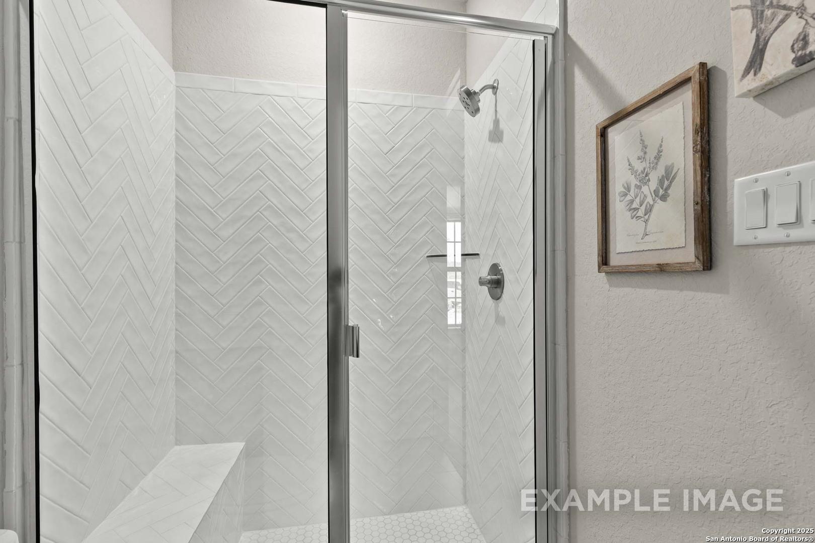 Elegant frameless glass shower with white herringbone tile, built-in bench, master bath in The Summerlin B by Davidson Homes, Castroville TX