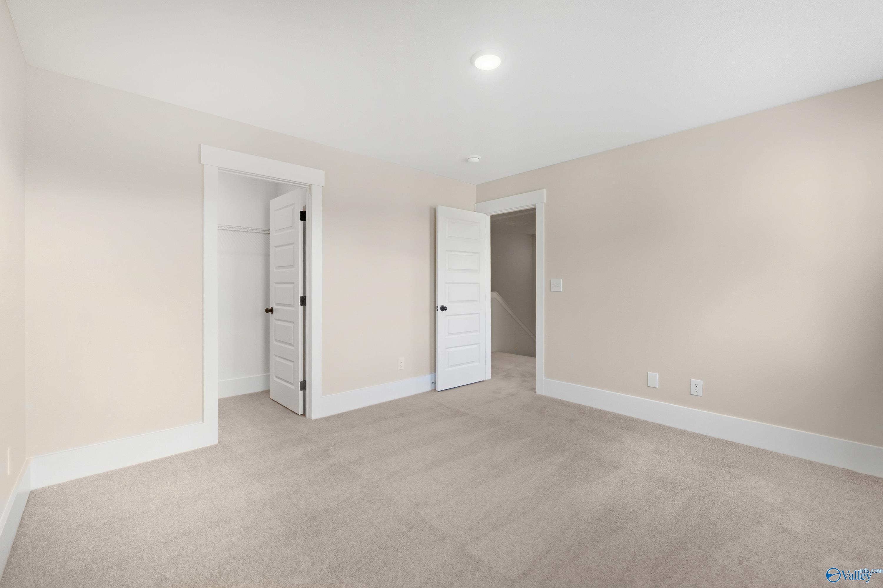 Spacious secondary bedroom with beige walls, neutral carpet, and double doors in Davidson Homes The Shelby A, Athens, Alabama