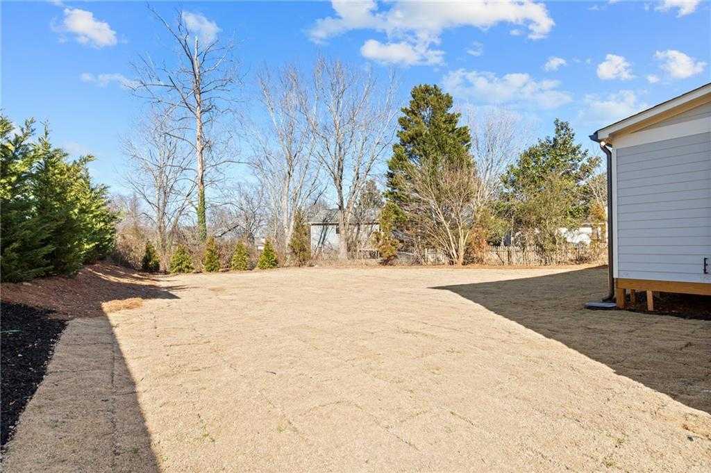 Newly sodded backyard with mulch borders, evergreen trees, and bare deciduous trees beside white-sided home in Tanglewood, East Cobb