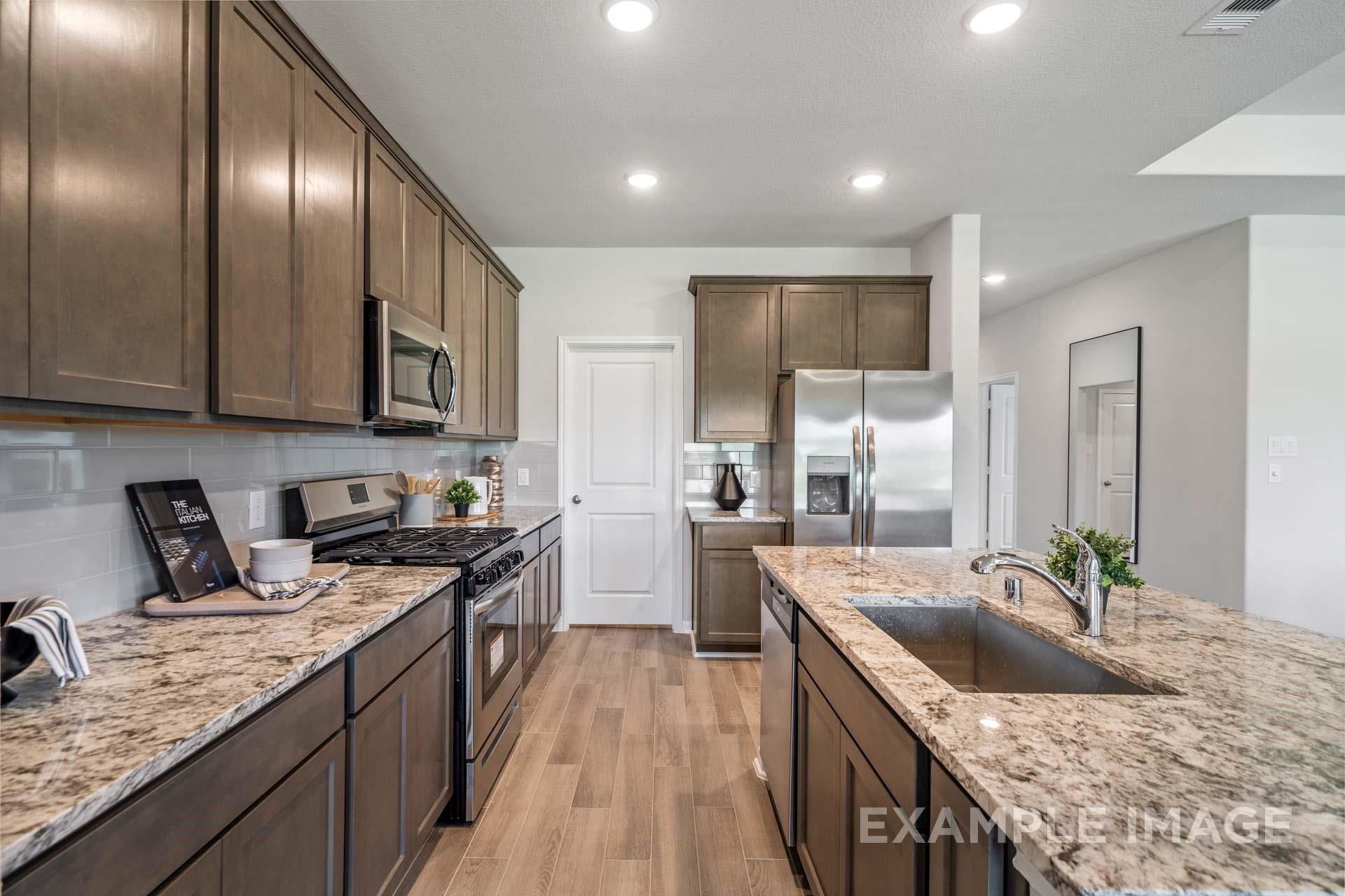 Modern kitchen with granite countertops, stainless appliances, and wood-look tile flooring in Davidson Homes Acadia A plan, Lago Mar Texas City