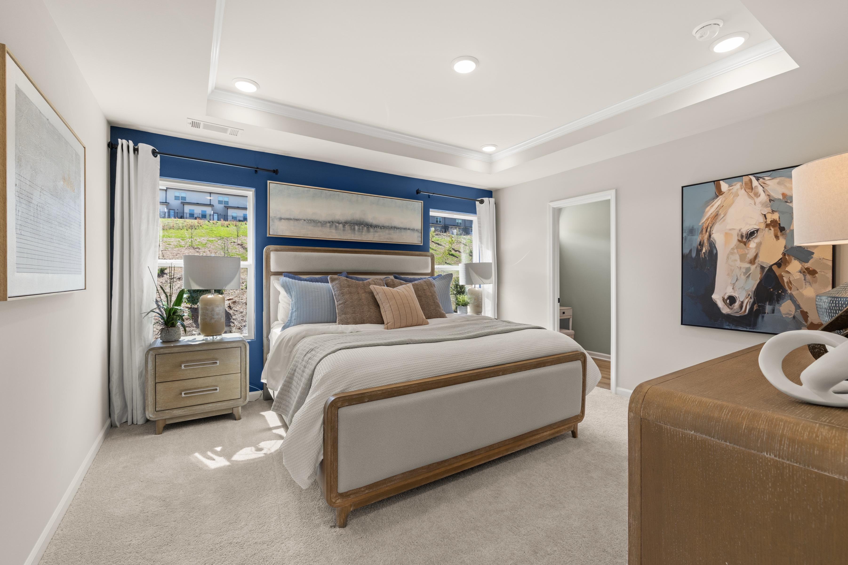 Spacious primary bedroom at The Bluffs in Canton GA with navy accent wall, king bed, abstract art, and large windows