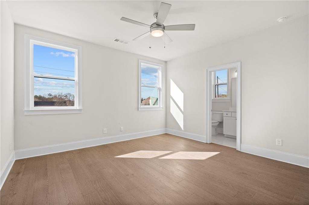 Sunny bedroom with hardwood floors, ceiling fan, large windows, and adjacent bath in Davidson Homes The Arlington A, East Cobb, Georgia