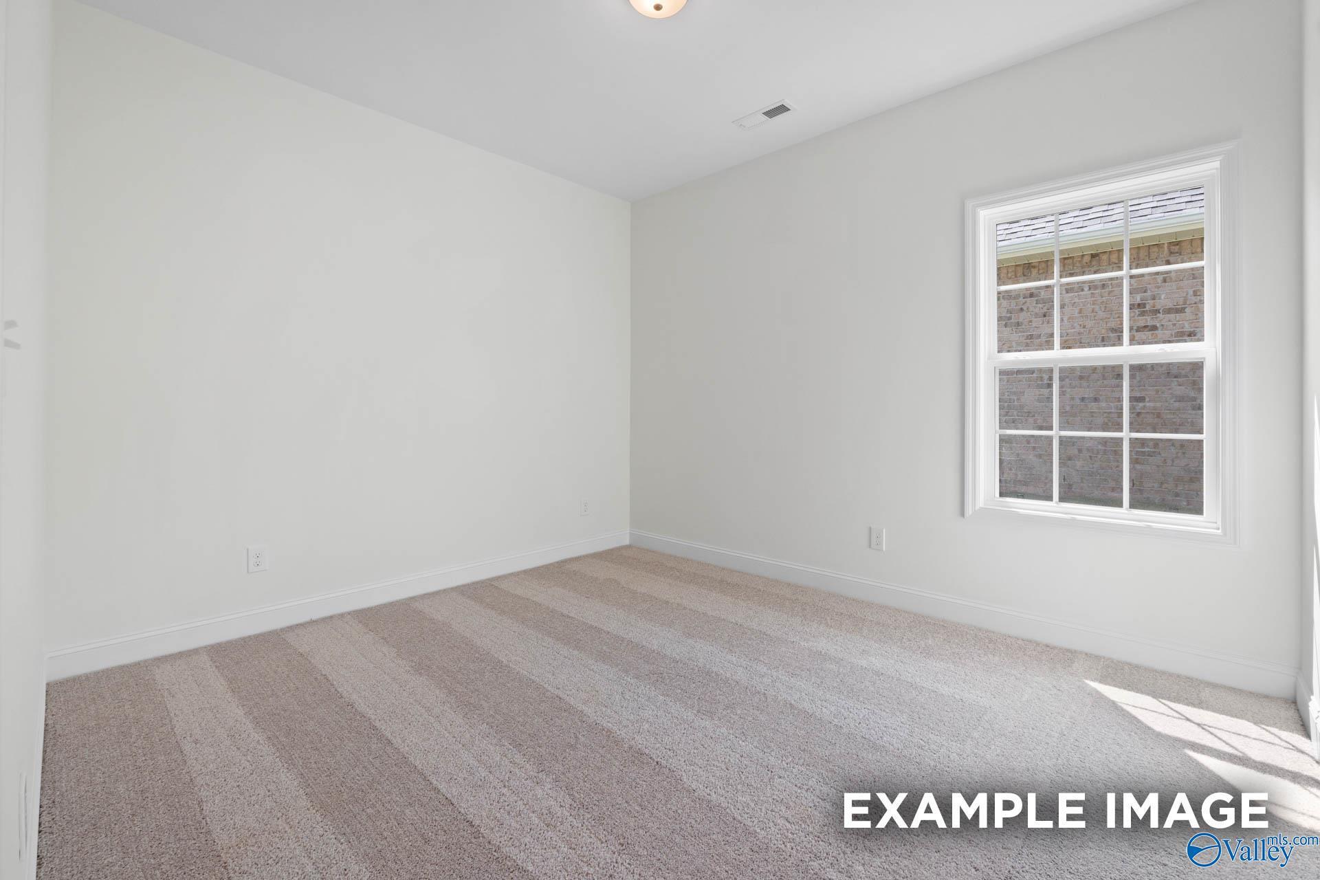 Bright empty bedroom with white walls, large window, and plush beige carpet in Davidson Homes The Rockford B, Athens Alabama