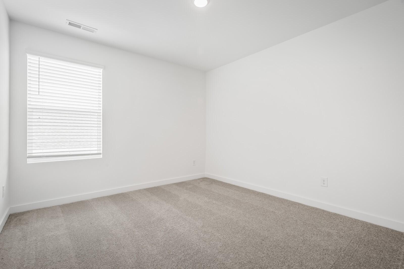 Empty secondary bedroom with white walls, blinds-covered window, and beige carpet in The Gordon C home, Sage Farms, White House, TN