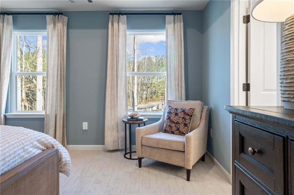 Bright bedroom with upholstered bed, accent chair by large windows overlooking woods, in Davidson Homes The Marion B, Kennesaw, Georgia