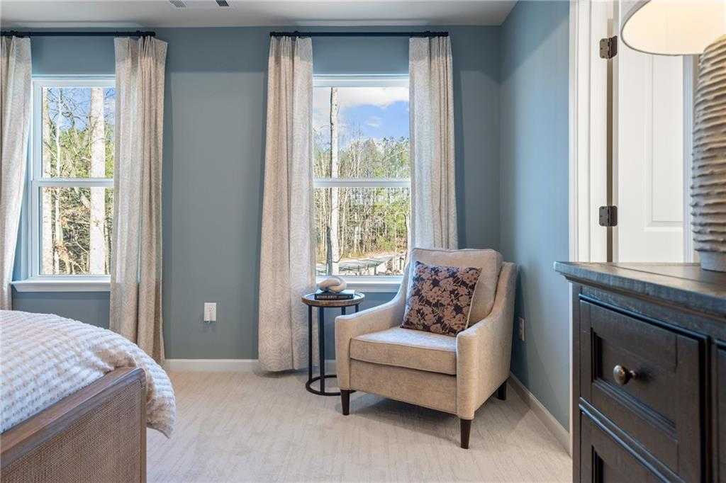 Cozy master bedroom with large windows, beige armchair, and dark wood dresser in Davidson Homes The Marion C, Winder, Georgia
