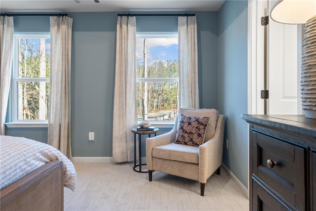 Bright bedroom with upholstered bed, accent chair by large windows overlooking woods, in Davidson Homes The Marion B, Kennesaw, Georgia