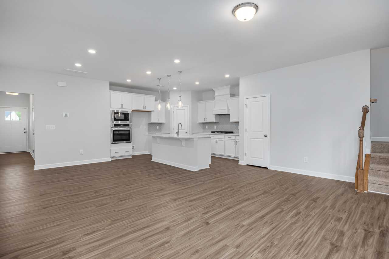 Spacious open-concept kitchen in The Durham home with white cabinets, large island, double ovens, and hardwood floors