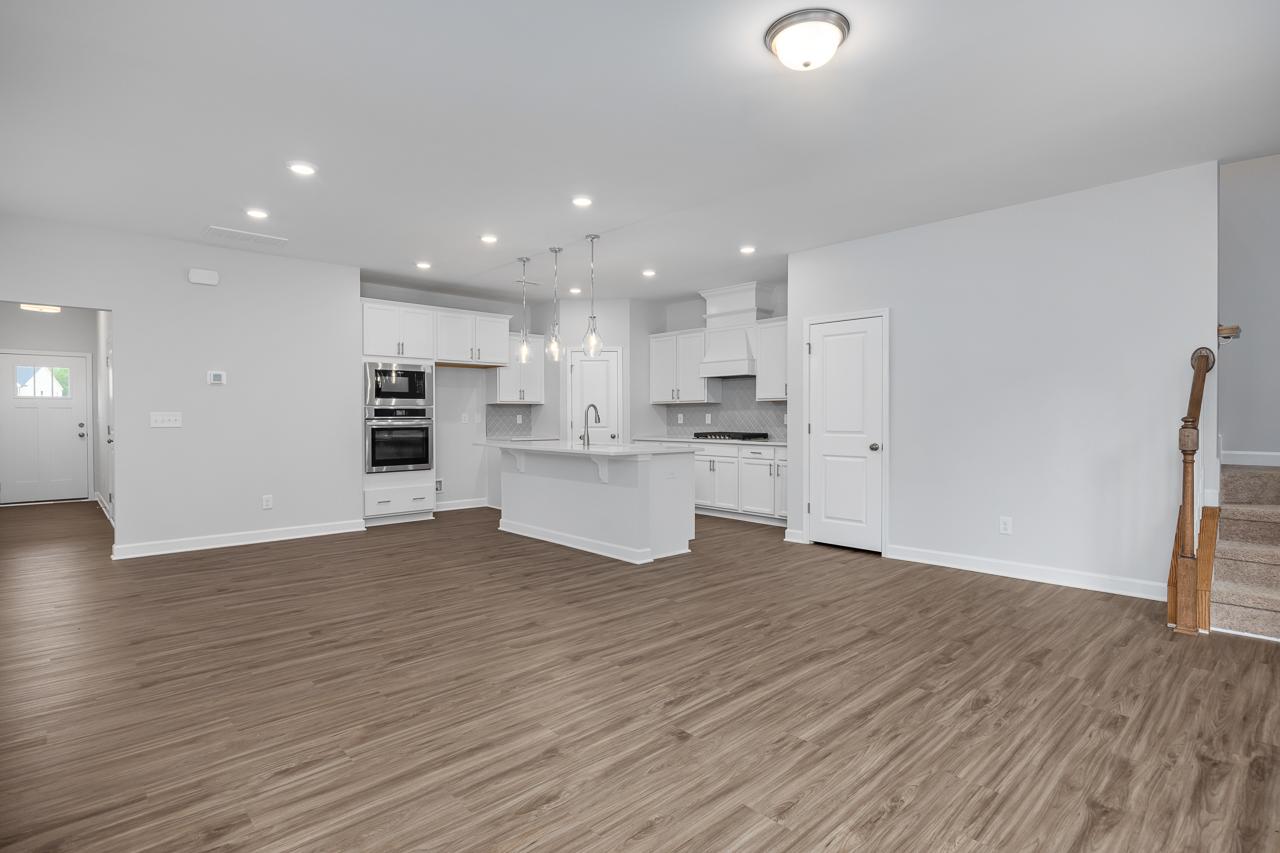 Spacious open-concept kitchen in The Durham C with white cabinets, large island, double ovens, recessed lighting, and hardwood floors