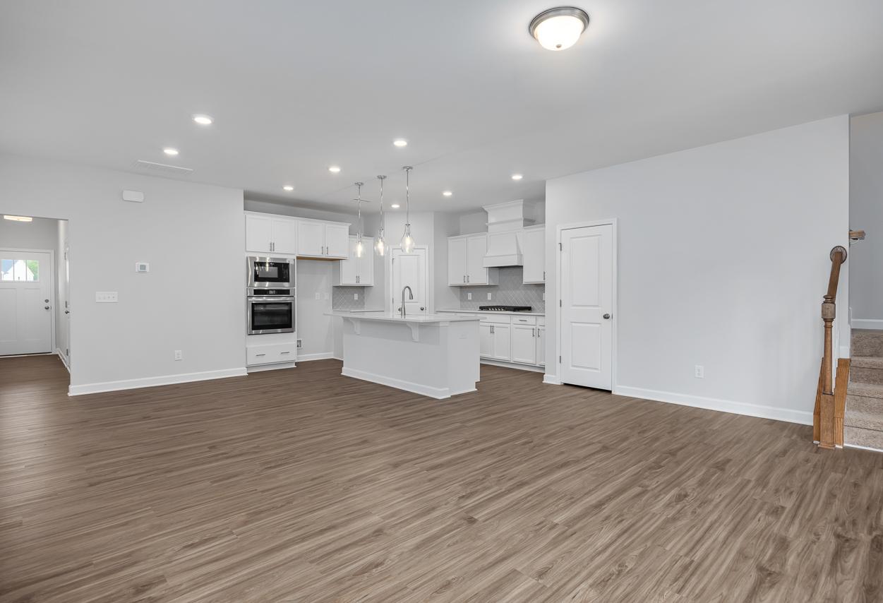 Spacious open-concept kitchen in The Durham C with white cabinets, large island, double ovens, recessed lighting, and hardwood floors
