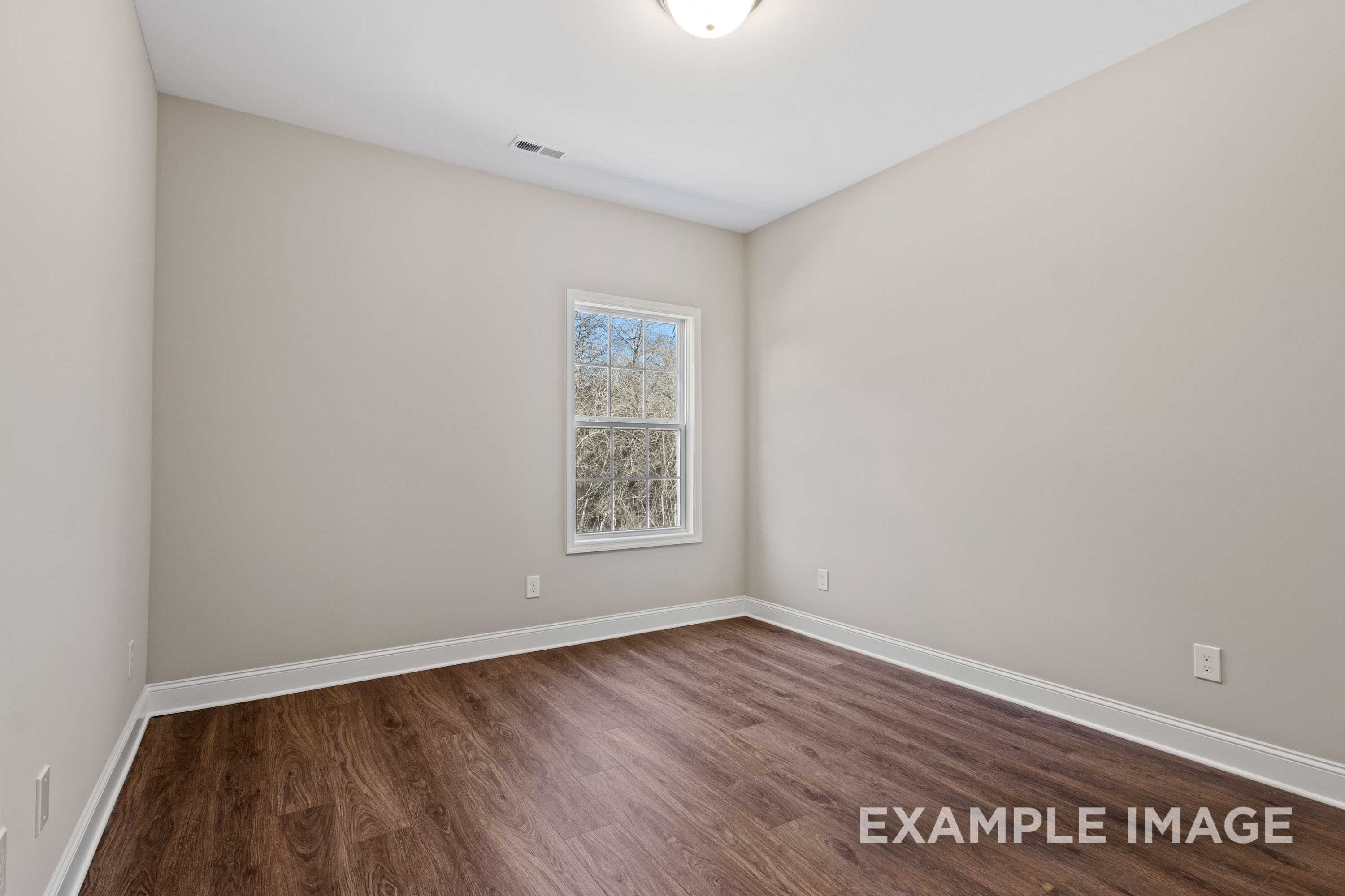 Spacious secondary bedroom in The Madison A by Davidson Homes with beige walls, hardwood floors, large window