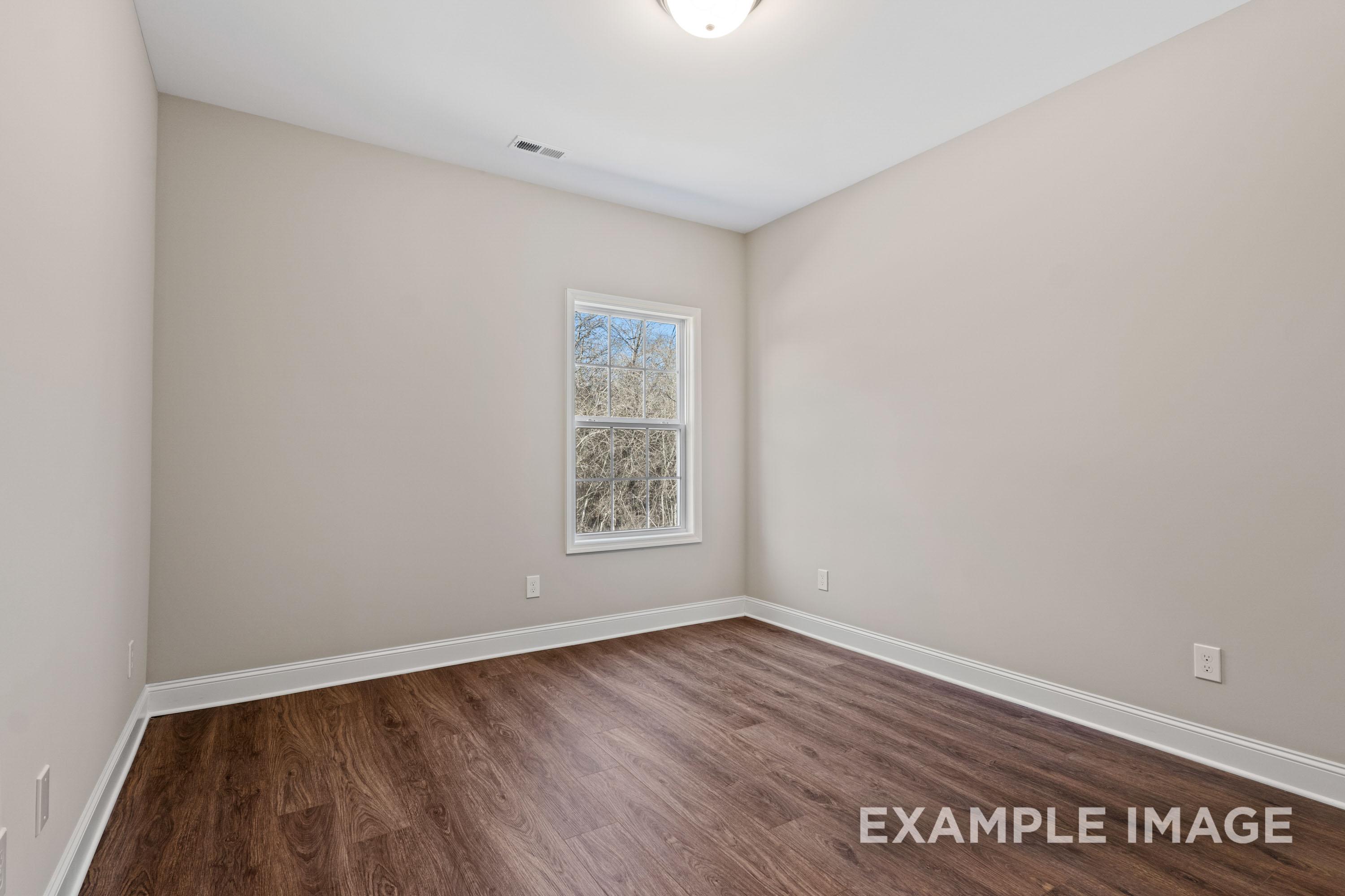 Spacious secondary bedroom in The Madison B with beige walls, hardwood floors, large window, and ceiling light