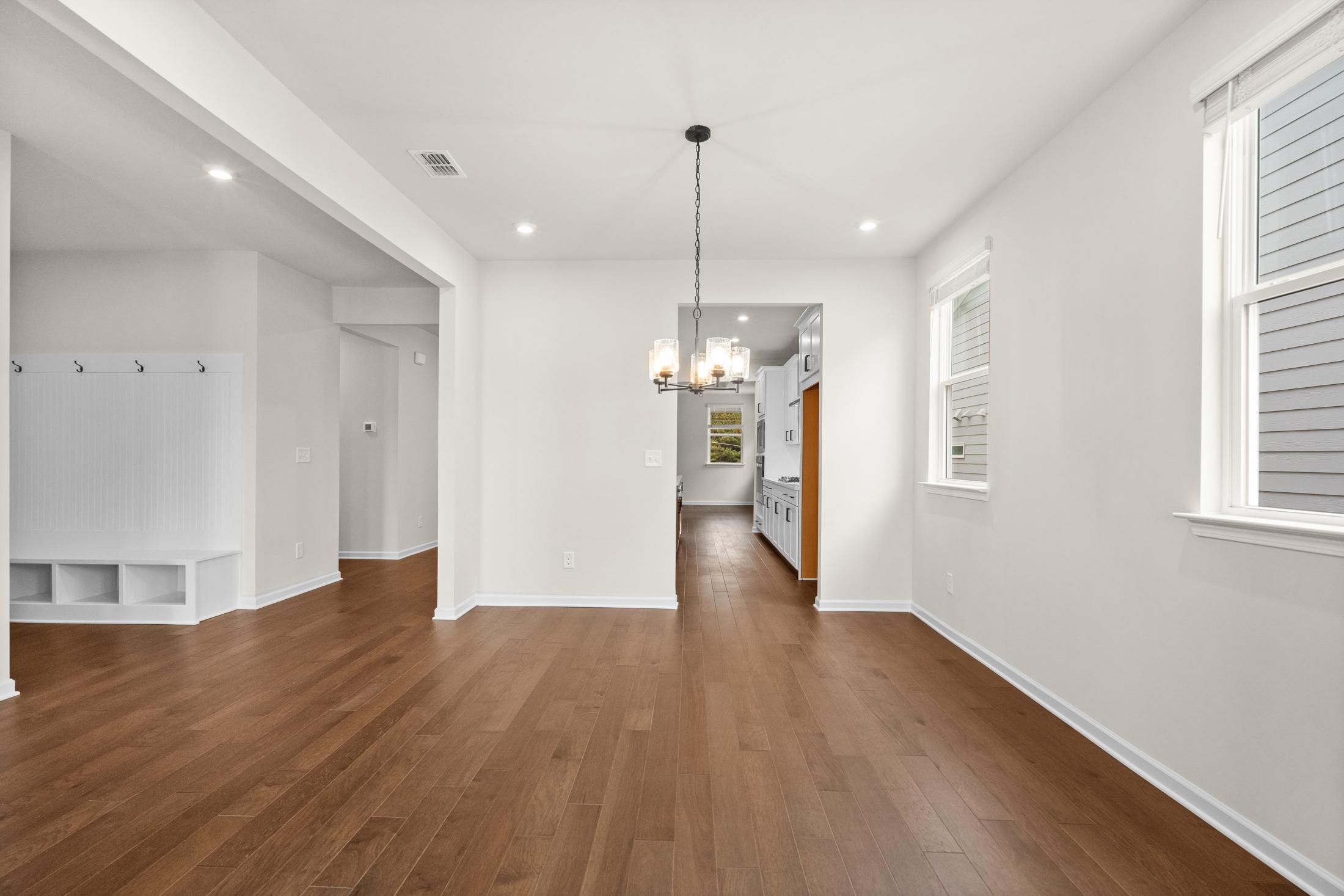 Spacious open-concept living room in The Glenwood with hardwood floors, white walls, chandelier, and kitchen view, Davidson Homes