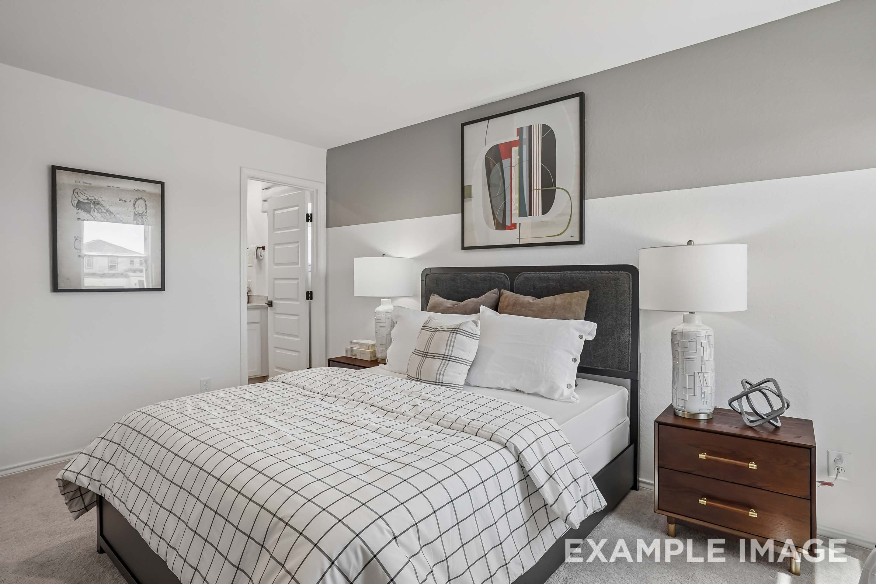 Modern bedroom suite in The Pinecrest D floor plan featuring a plaid duvet, upholstered headboard, and wood nightstands.