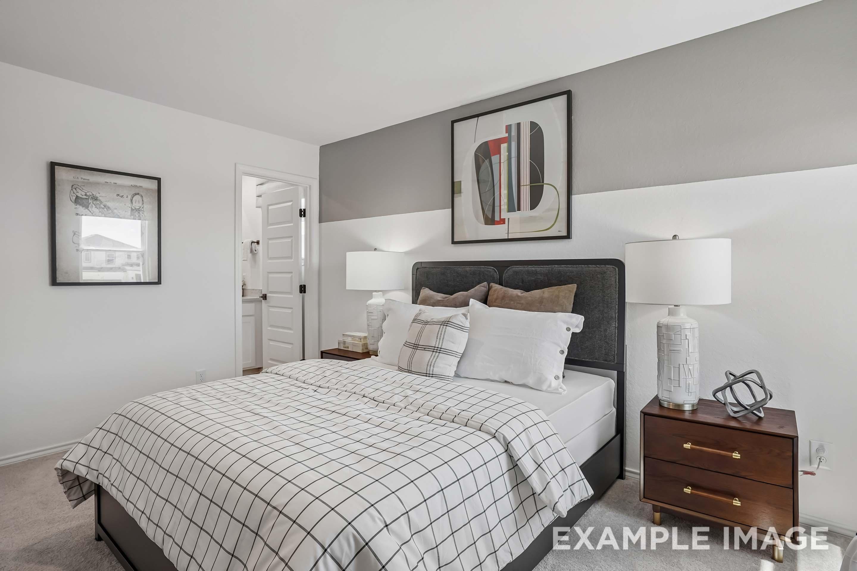 Modern bedroom suite in The Pinecrest D floor plan featuring a plaid duvet, upholstered headboard, and wood nightstands.