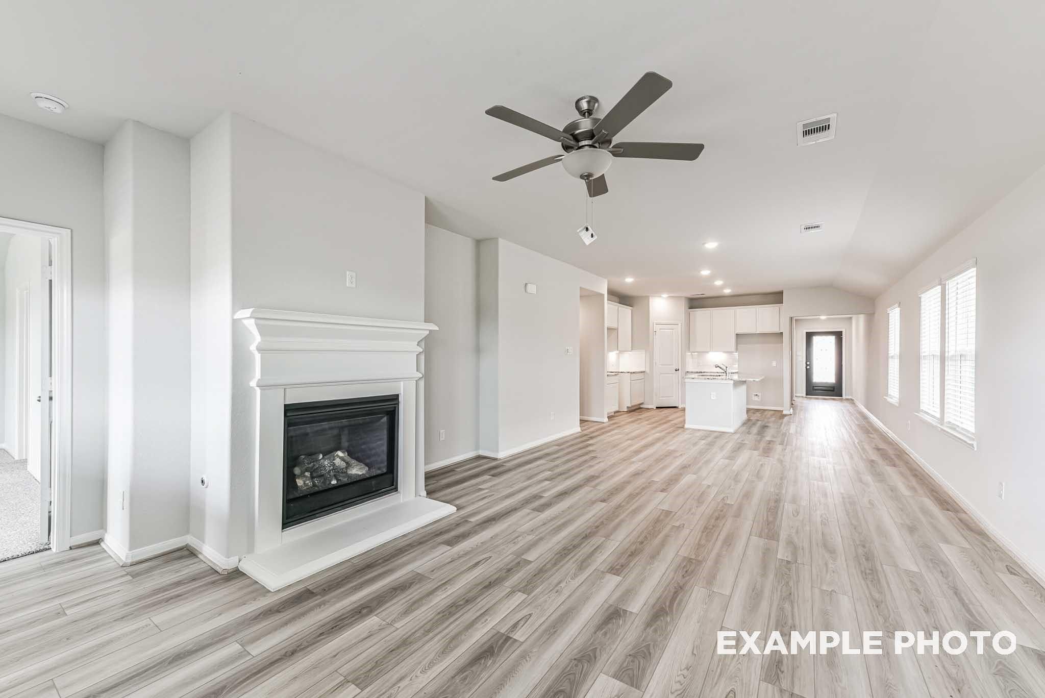 Open living room with white brick fireplace, open kitchen island, and luxury vinyl plank floors in Davidson Homes The Riviera A, Rosharon, Texas