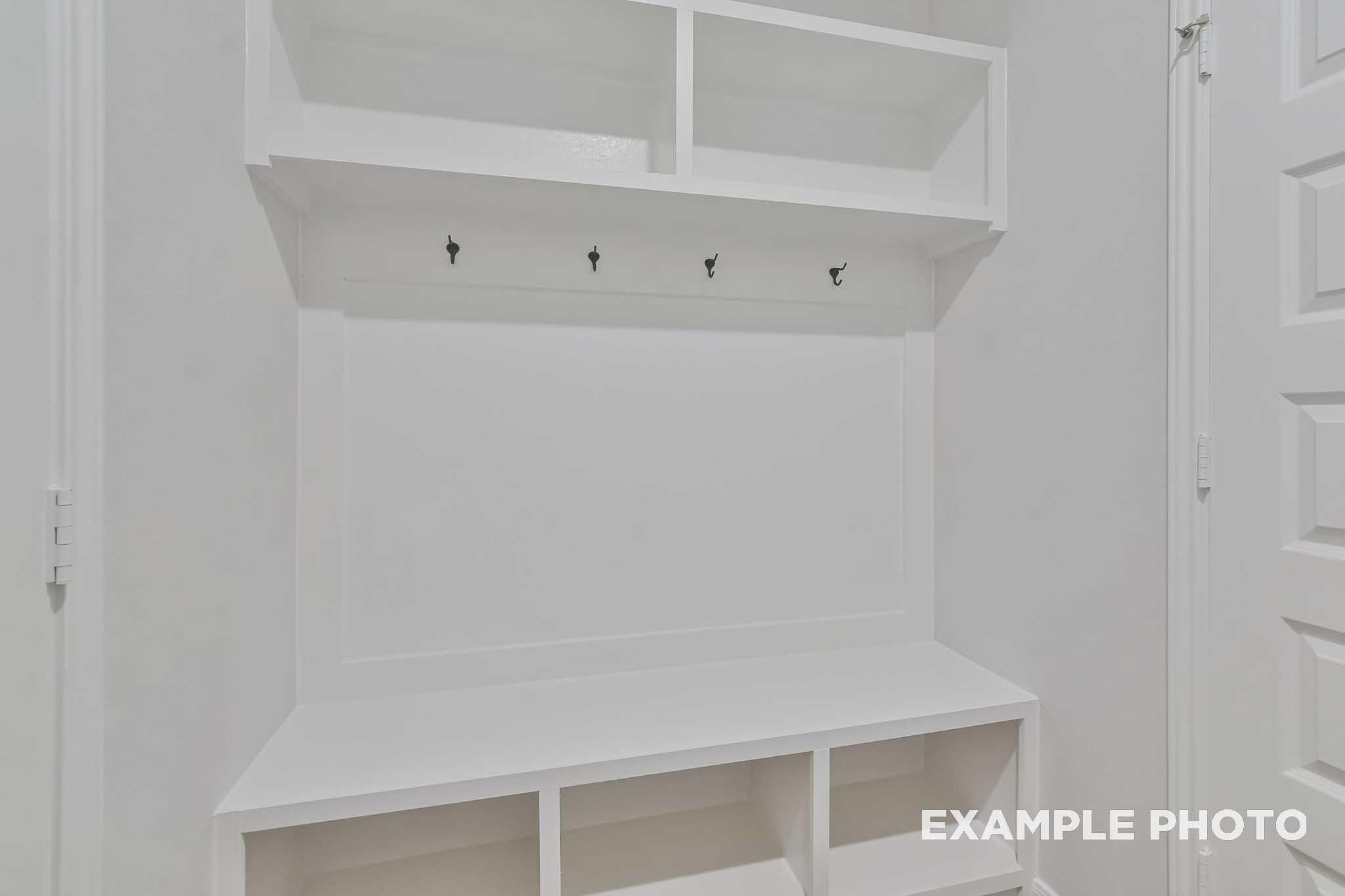 White built-in mudroom with coat hooks, shelves, and bench in Davidson Homes The Frio F, Conroe, Texas
