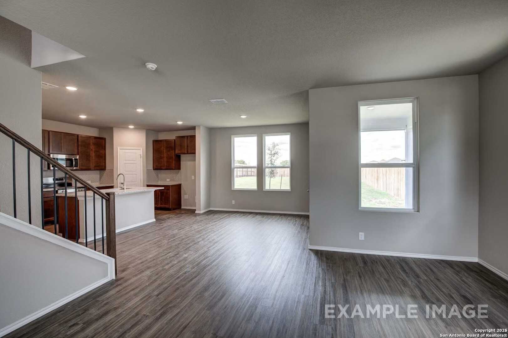 Open-concept living area with laminate floors, modern kitchen island, and staircase in Davidson Homes The Murray K, San Antonio, TX