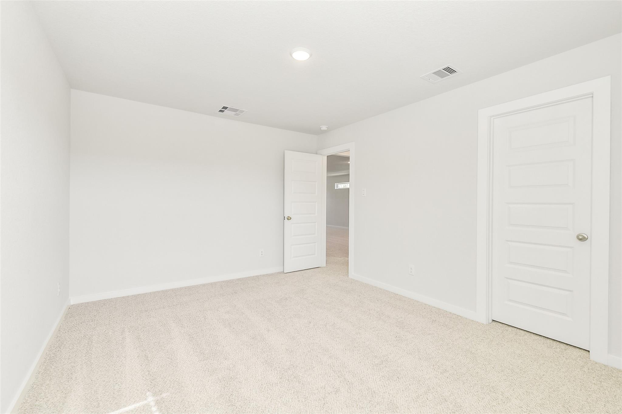 Bright secondary bedroom with beige carpet, white walls, and open door to hallway in Davidson Homes San Marcos E, Cleveland, Texas