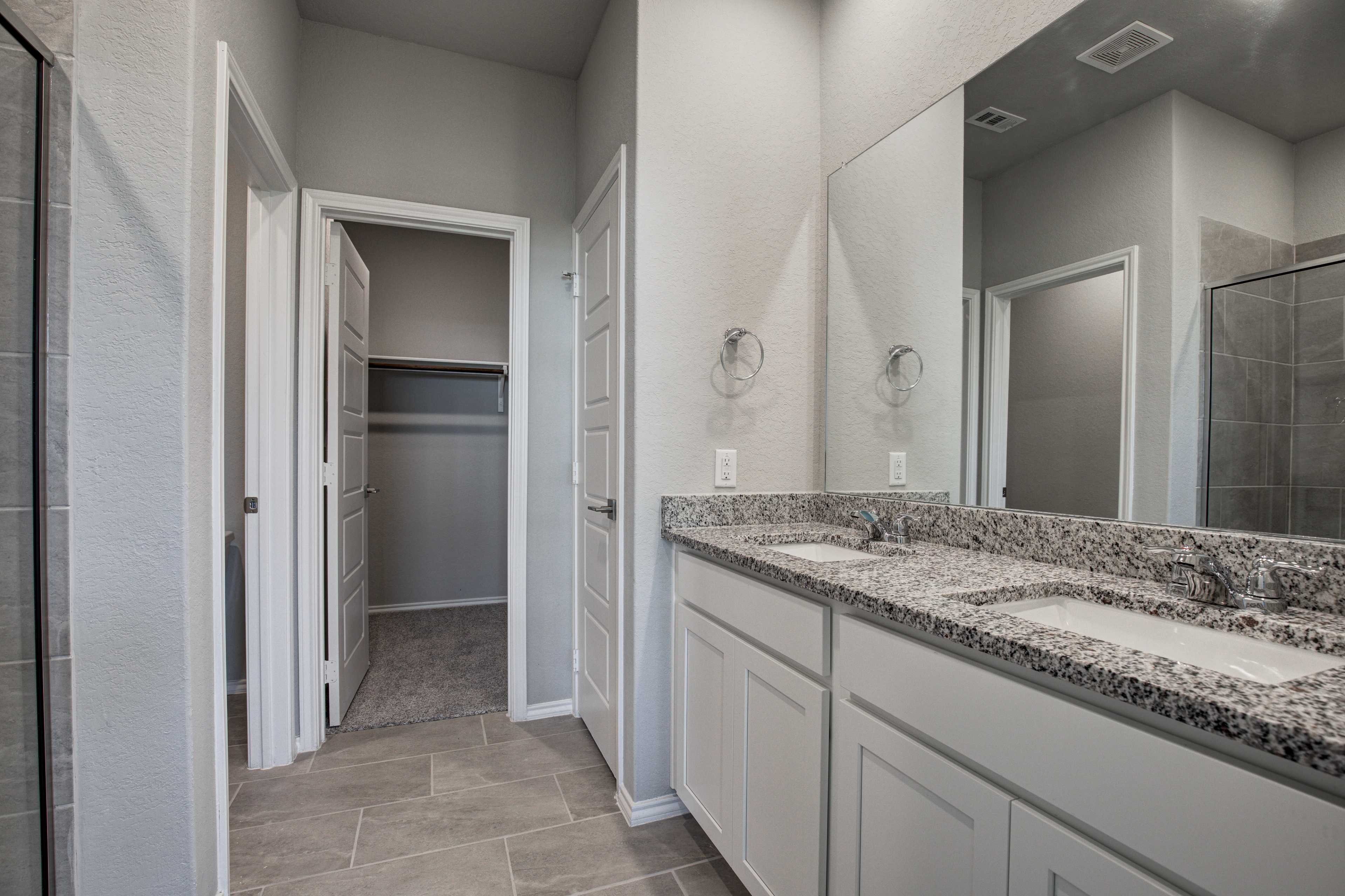 Spacious master bathroom in The Asheville featuring double vanity, granite counters, walk-in closet, and glass shower