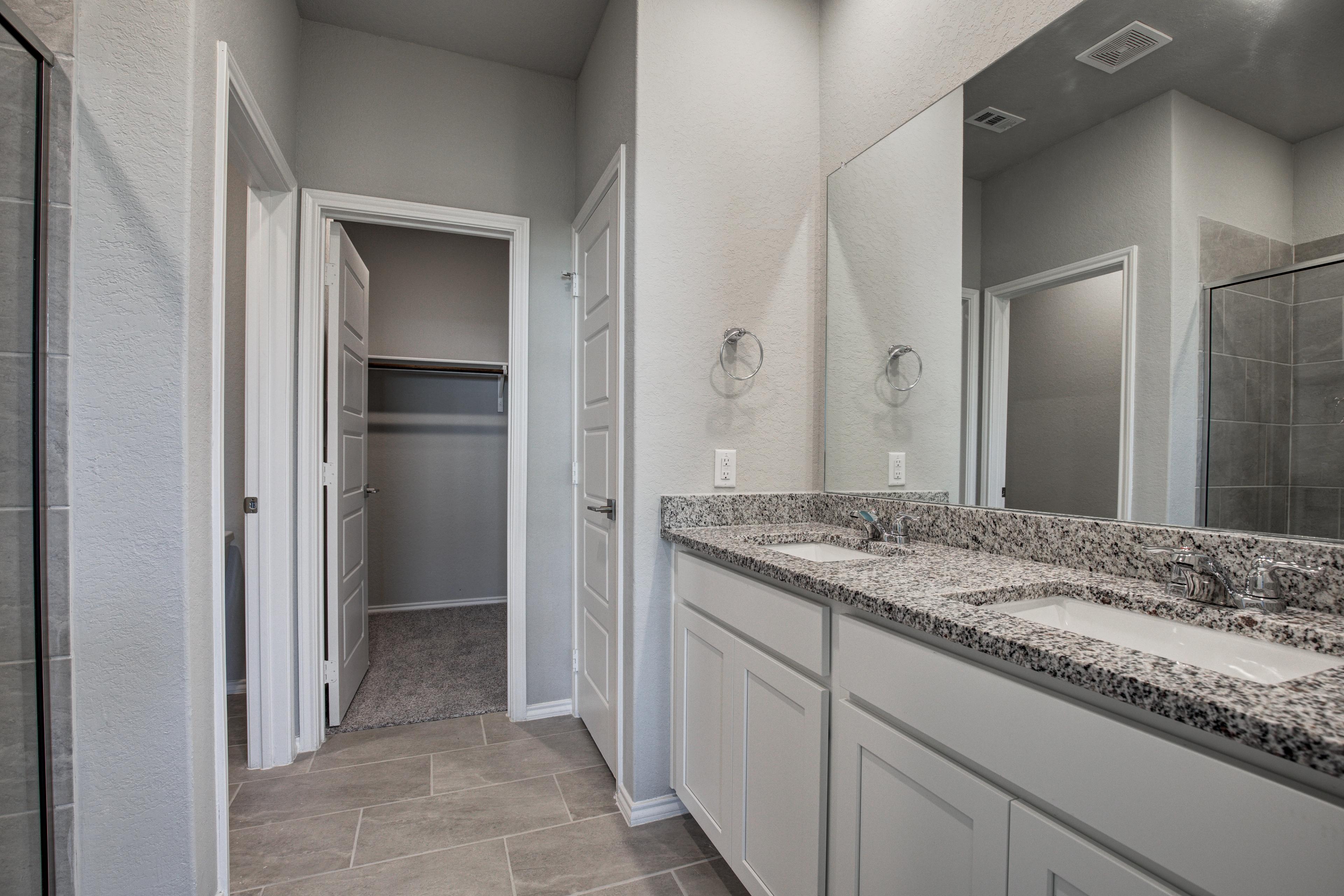 Spacious master bathroom in The Asheville with double vanity, granite counters, white cabinets, and open walk-in closet