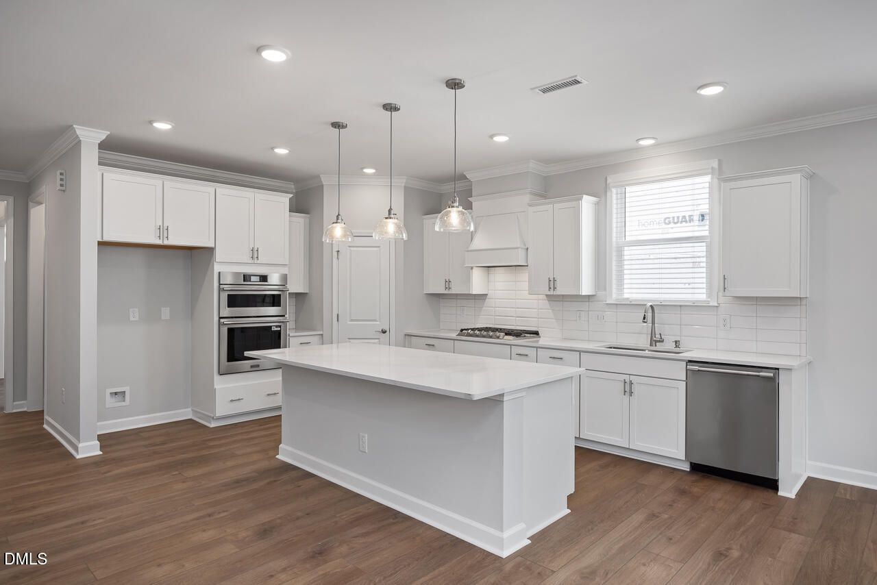 Modern kitchen with white cabinets, quartz island, and stainless appliances in The Ashport L, Sage on North Main, Wake Forest