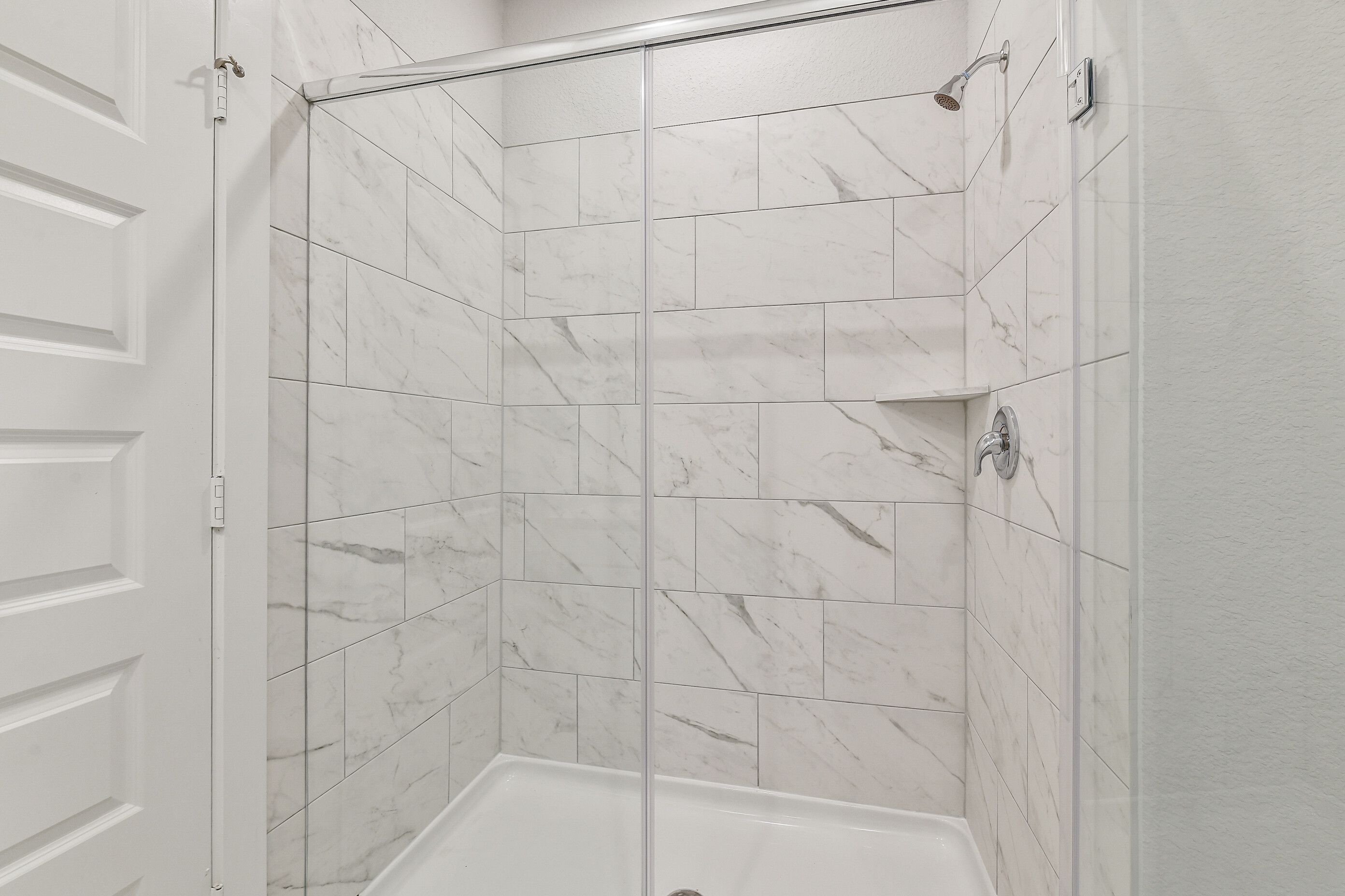 Elegant walk-in shower with frameless glass door, white marble subway tiles, and rain showerhead in Davidson Homes The Colorado G, Magnolia TX
