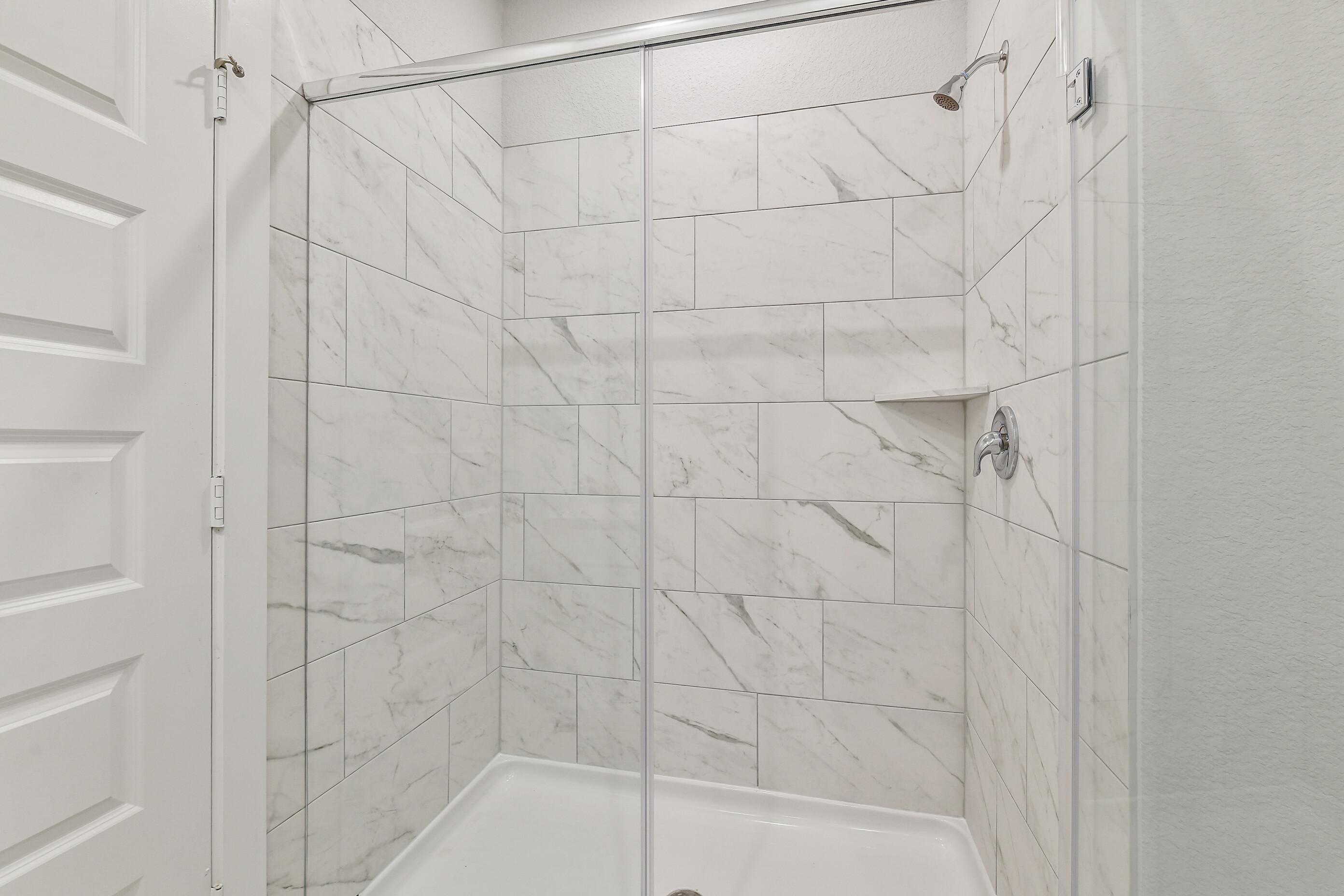 Elegant walk-in shower with frameless glass door, white marble subway tiles, and rain showerhead in Davidson Homes The Colorado G, Magnolia TX