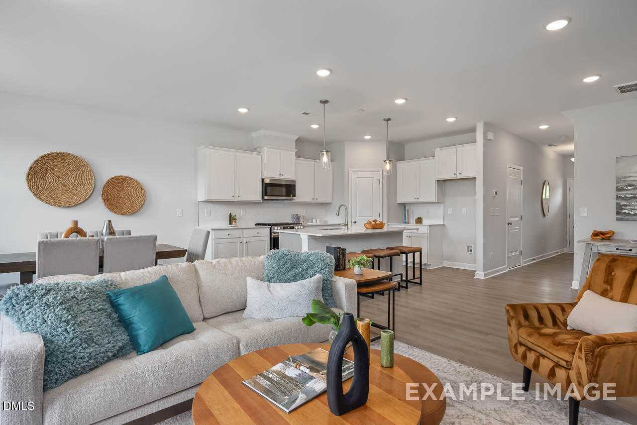 Modern open-concept living room with white sofa, teal pillows, wooden coffee table, and kitchen island in Davidson Homes The Warren, Fuquay-Varina