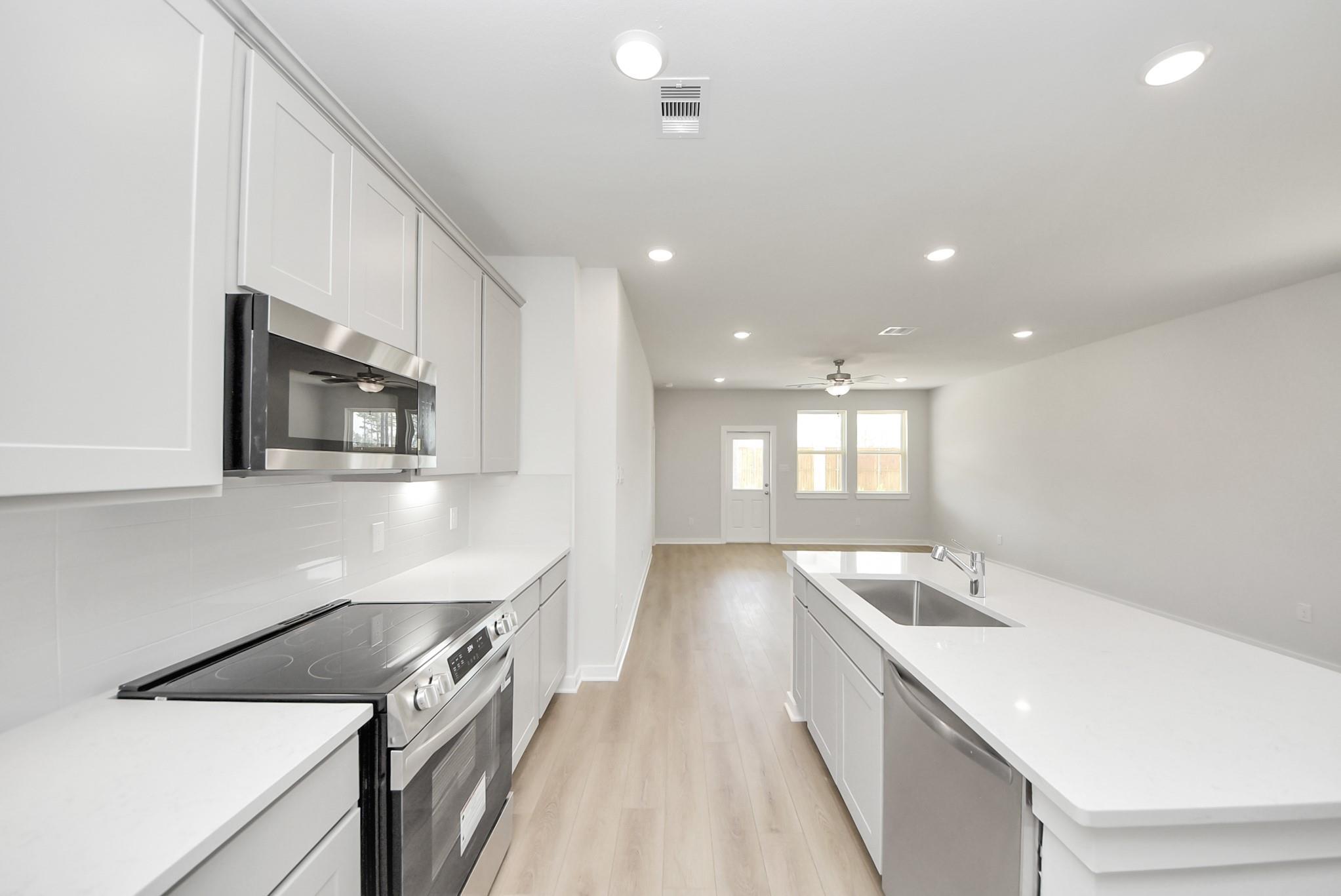 Modern open-concept kitchen with white cabinets and quartz island in The Blanco F floor plan, Spring Branch Crossing, Conroe.
