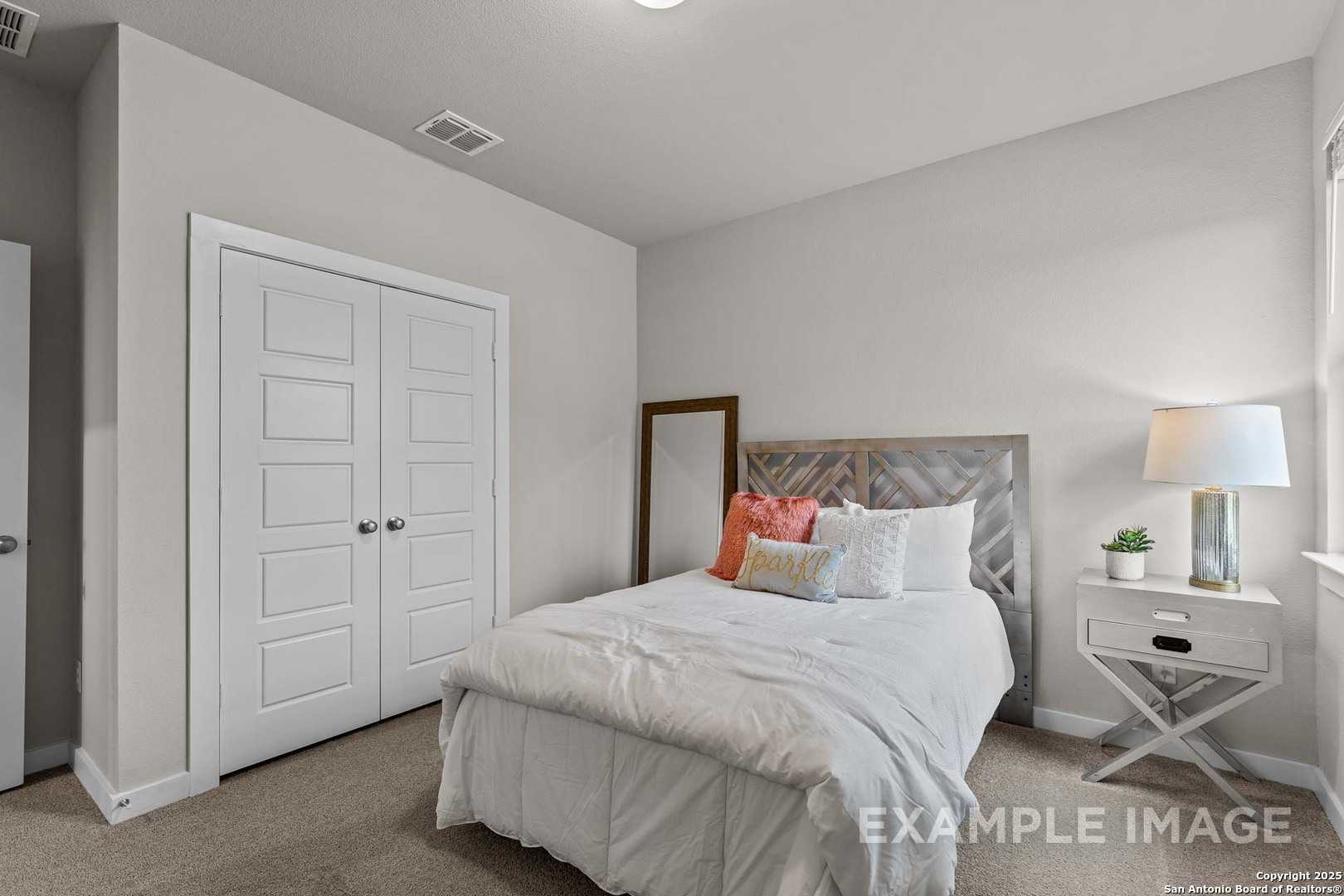 Cozy secondary bedroom with queen bed, gray upholstered headboard, colorful pillows, and double closet in Davidson Homes The Collin B, Seguin, Texas