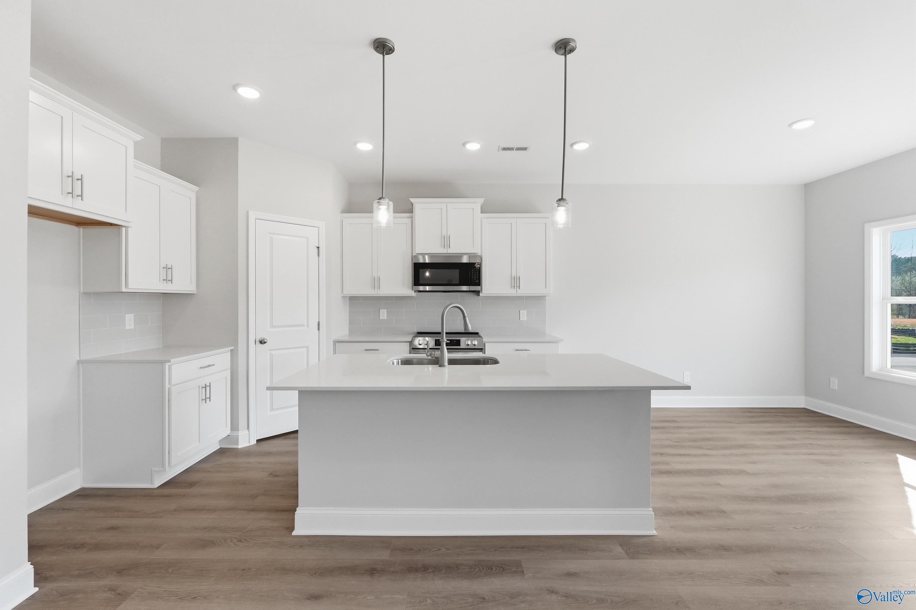 Modern white kitchen island with stainless sink and appliances, pendant lights, hardwood floors in The Asheville C, Huntsville, AL