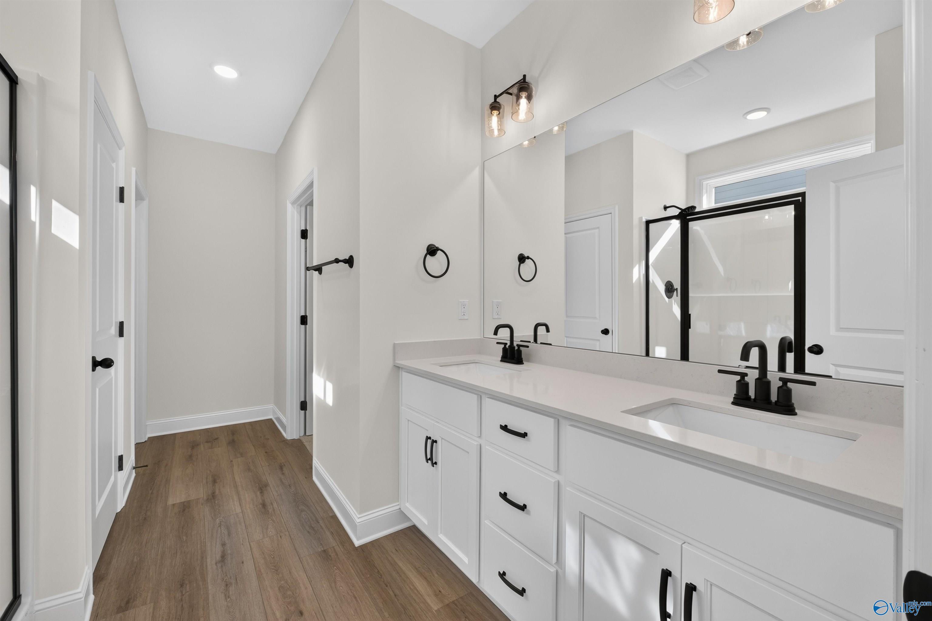Double vanity bathroom with white cabinets, matte black faucets, and wood-look flooring in Davidson Homes Ashport L, New Market, AL