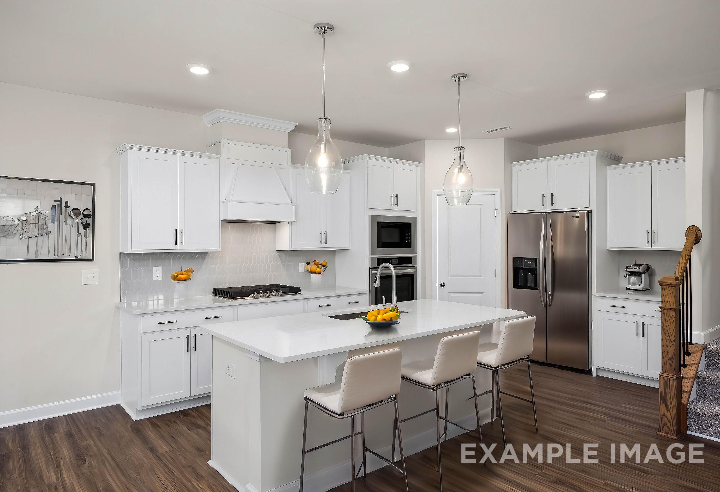 Bright kitchen in The Grace A home with white shaker cabinets, large quartz island, bar stools, stainless steel appliances, and pendant lights