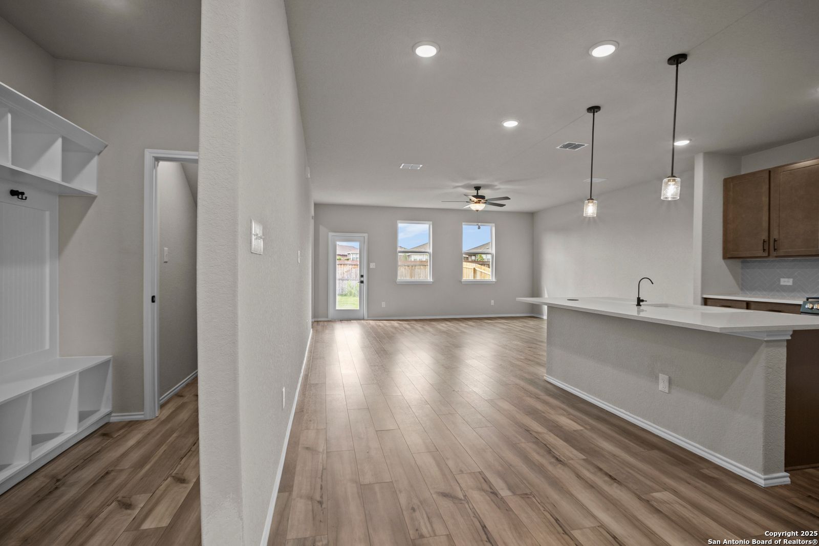 Open-concept living and kitchen with wood floors, white island, mudroom bench in Davidson Homes Douglas F, San Antonio