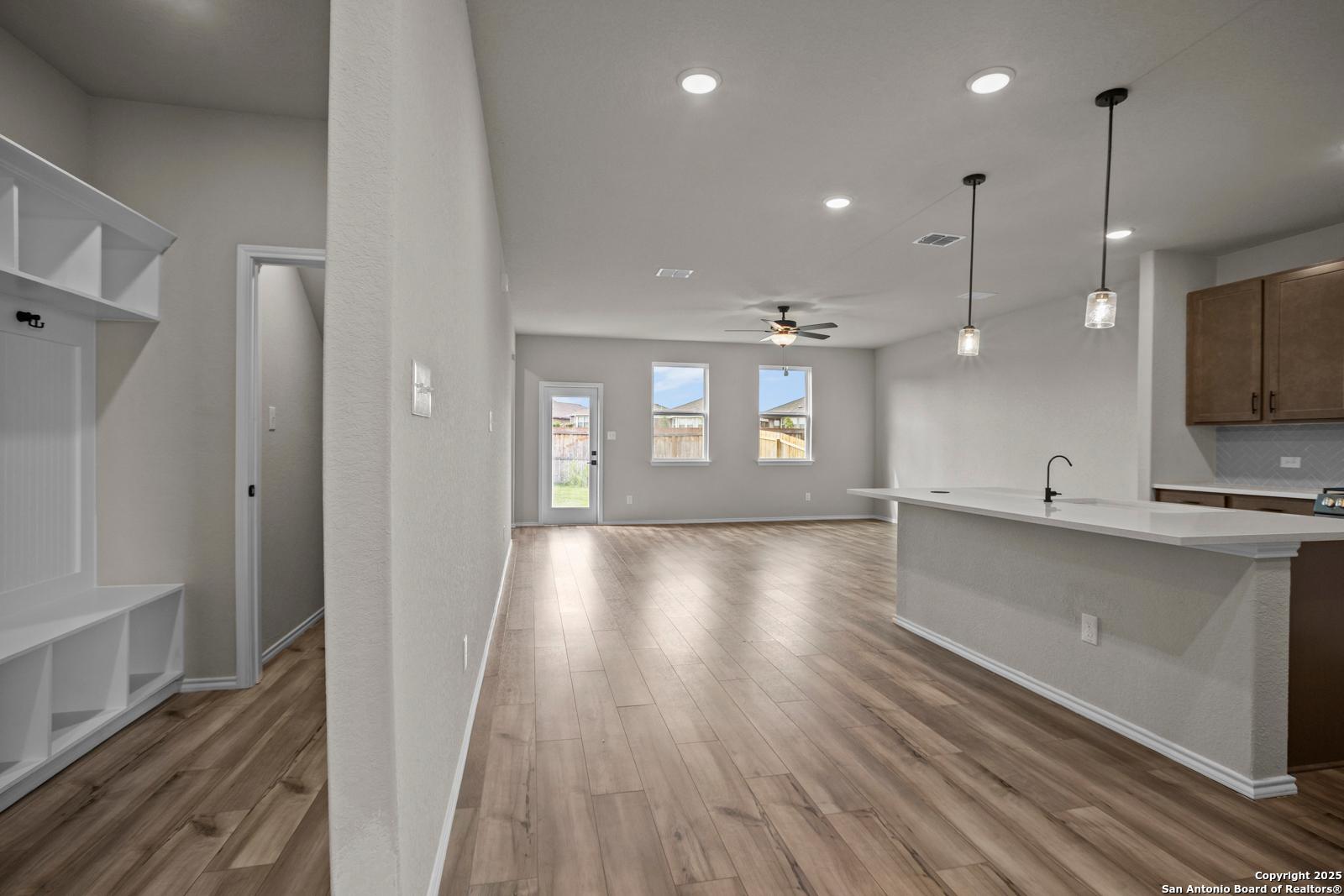 Open-concept living and kitchen with wood floors, white island, mudroom bench in Davidson Homes Douglas F, San Antonio