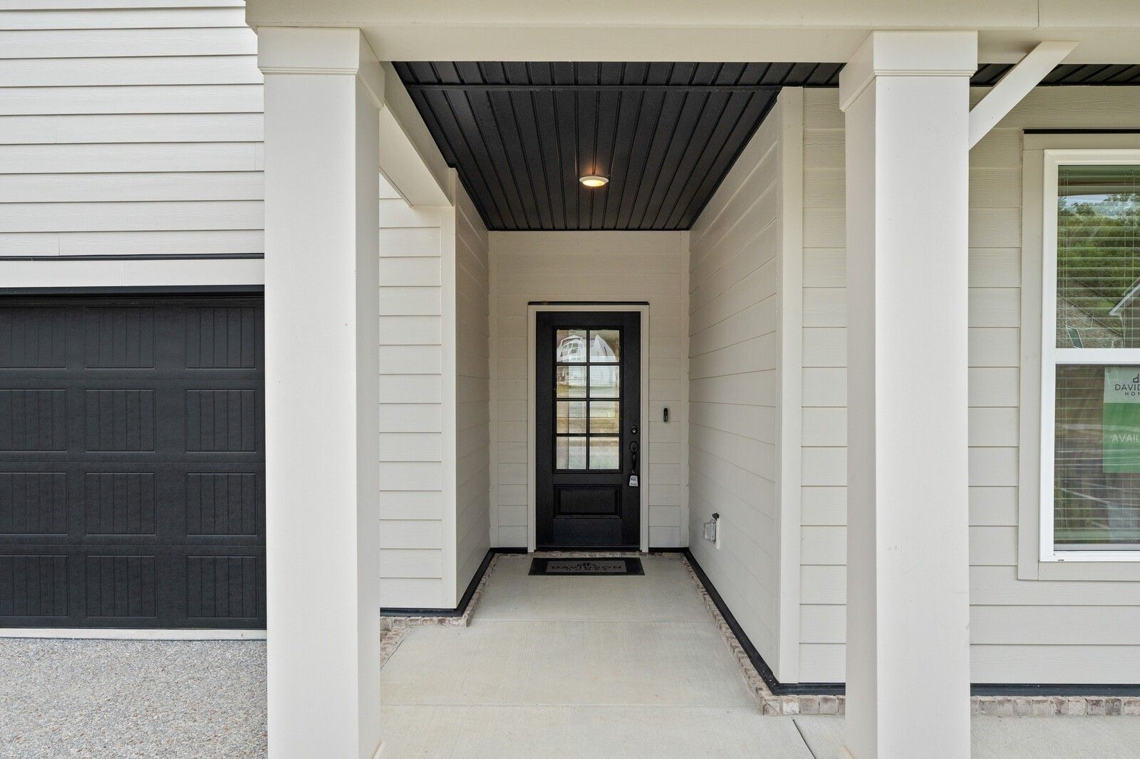 Welcoming covered front porch with columns, black entry door, and 2-car garage on 4-bedroom Davidson Homes Ridgeport in Carellton, Gallatin, Tennessee